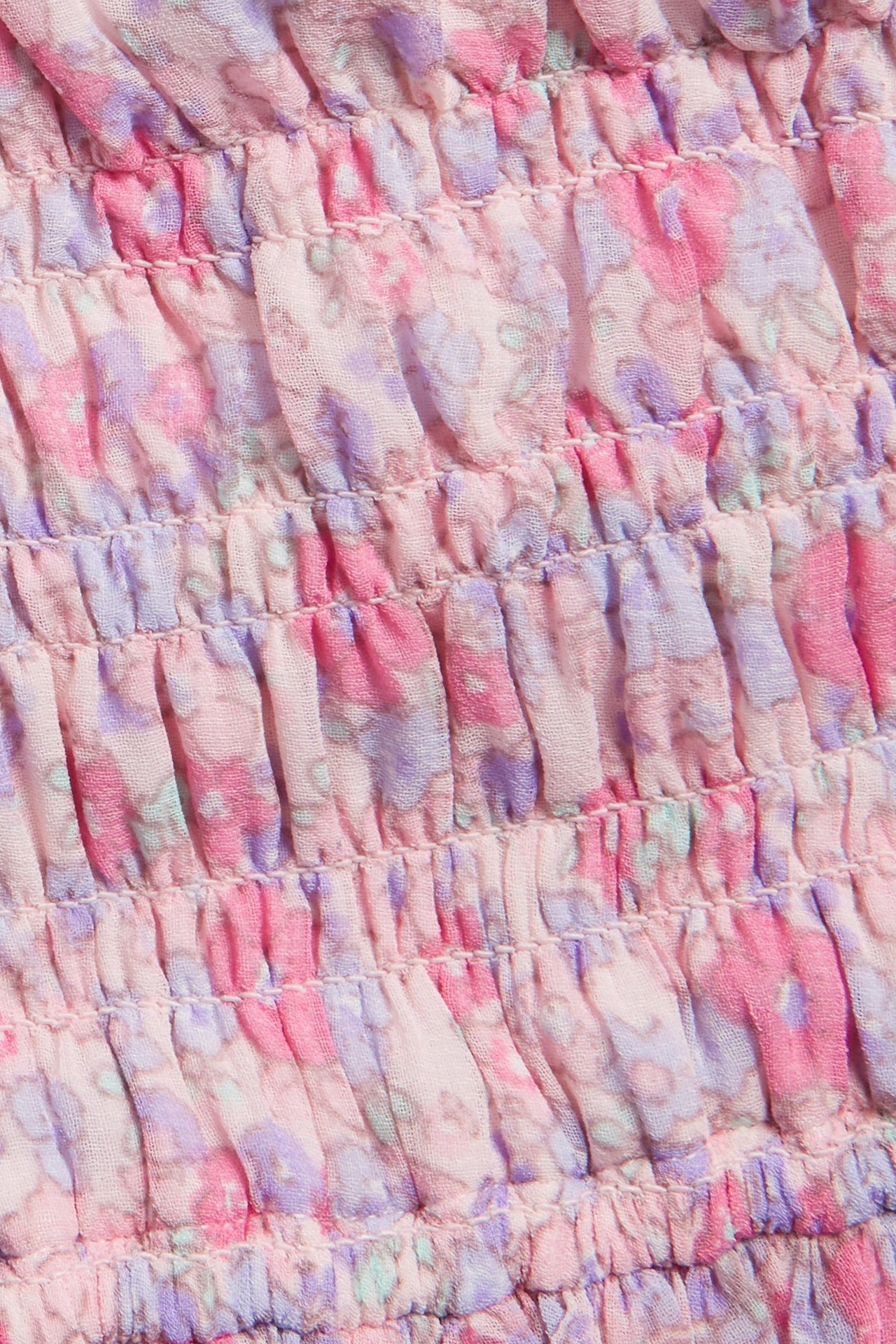 Zbliżenie różowej kwiecistej sukienki z szyfonu ze smockowanym stanikiem.