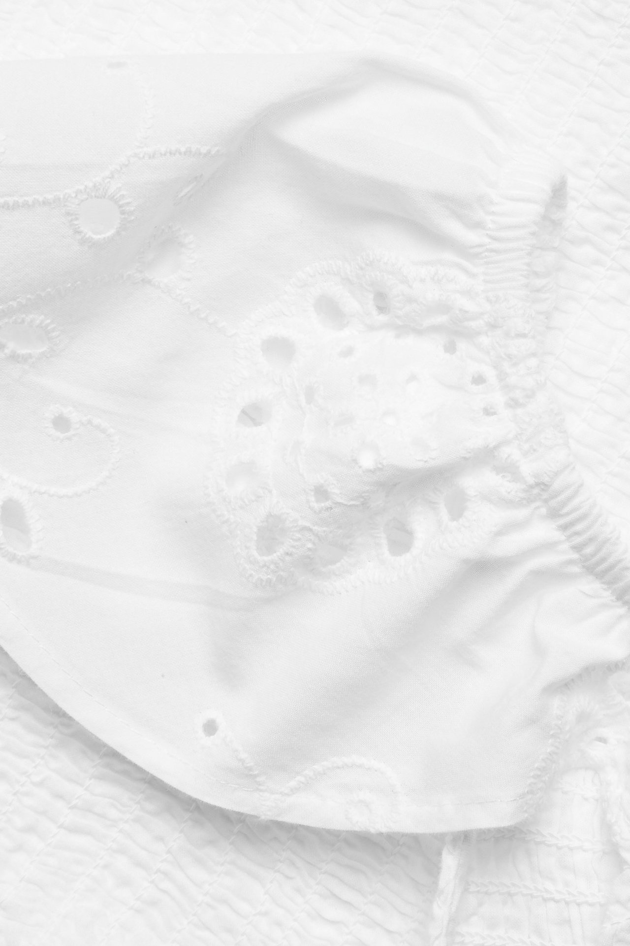 Zbliżenie białego bawełnianego topu z marszczeniami, falbanami z haftem angielskim i haftowanymi detalami.
