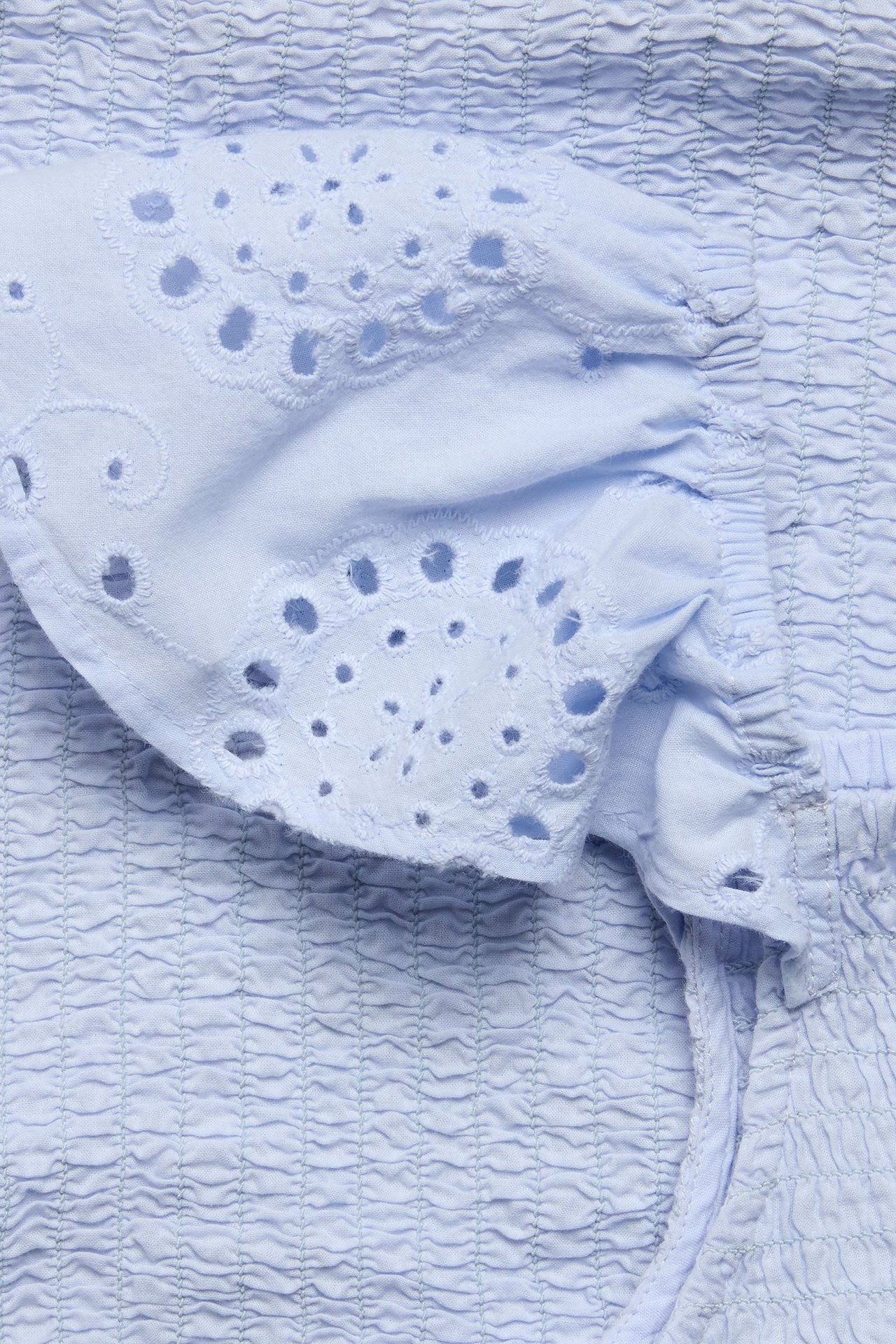 Zbliżenie na jasnoniebieski, marszczony bawełniany top z falbankami z haftu angielskiego.