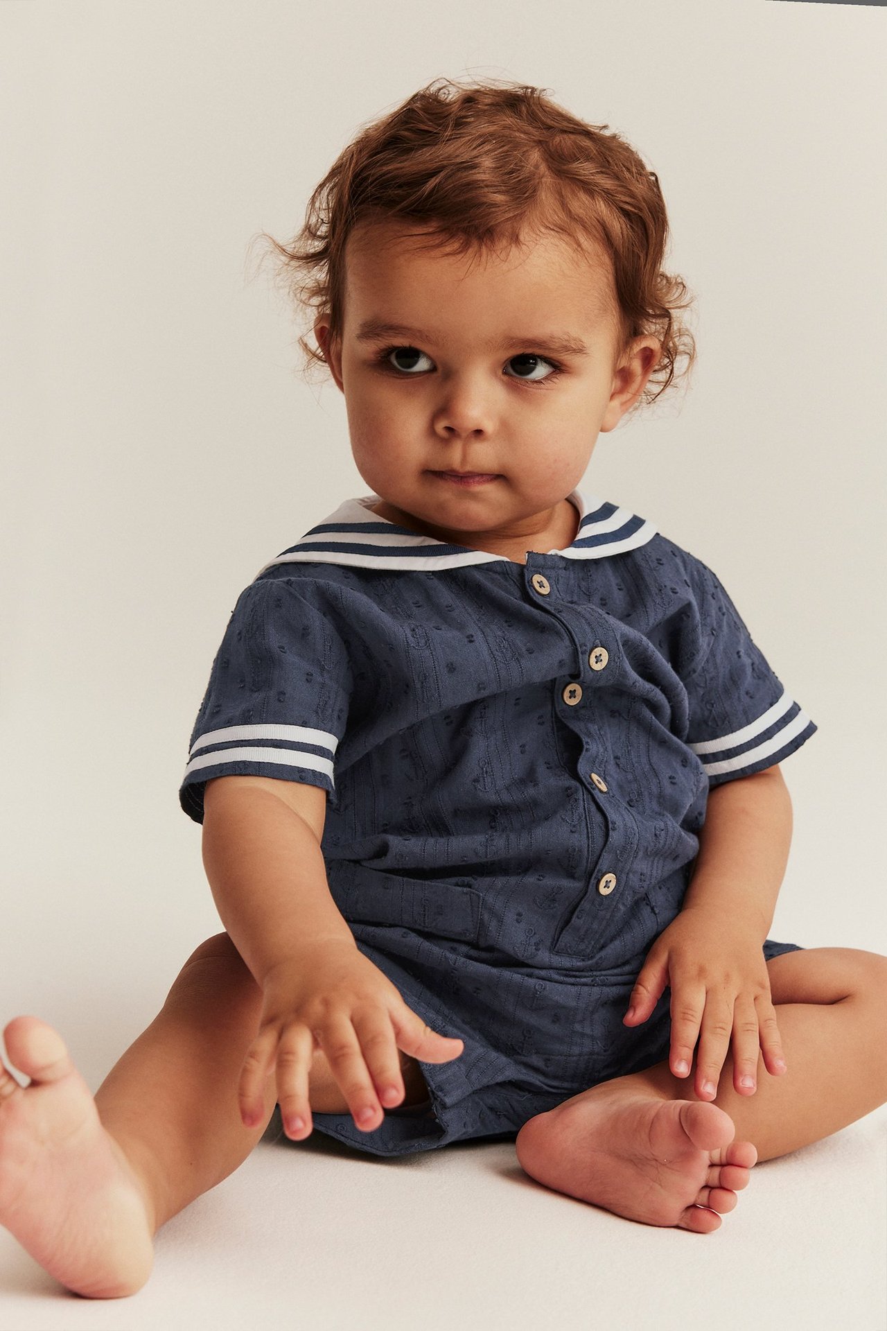 Edestä: vauva tummansinisessä kuviollisessa puuvillahaalarissa, jossa valkoinen raidallinen merimieskaulus.
