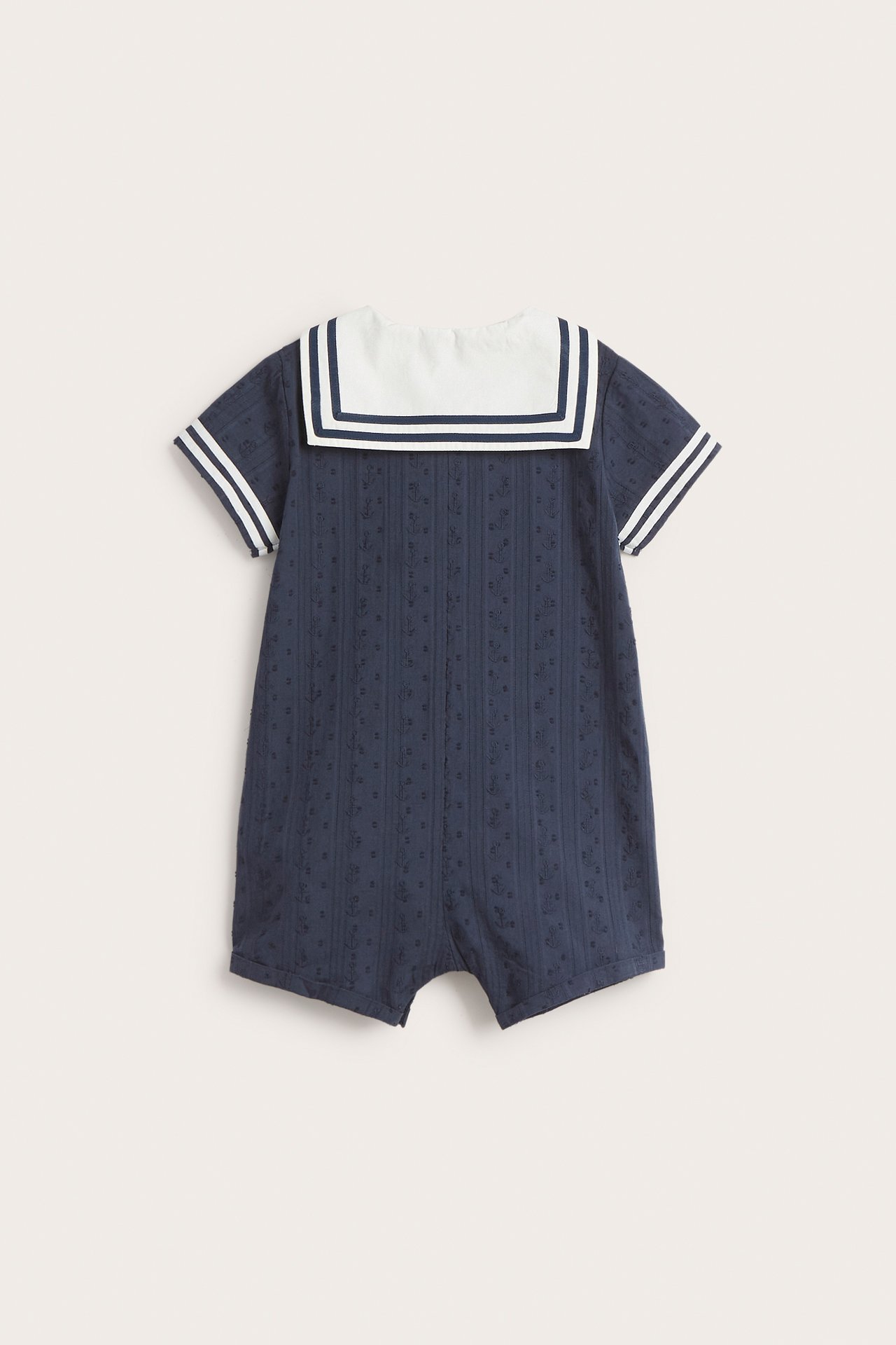 Takaa: vauvan tummansininen puuvillainen playsuit valkoisella merimieskauluksella ja raidallisilla lyhyillä hihoilla.