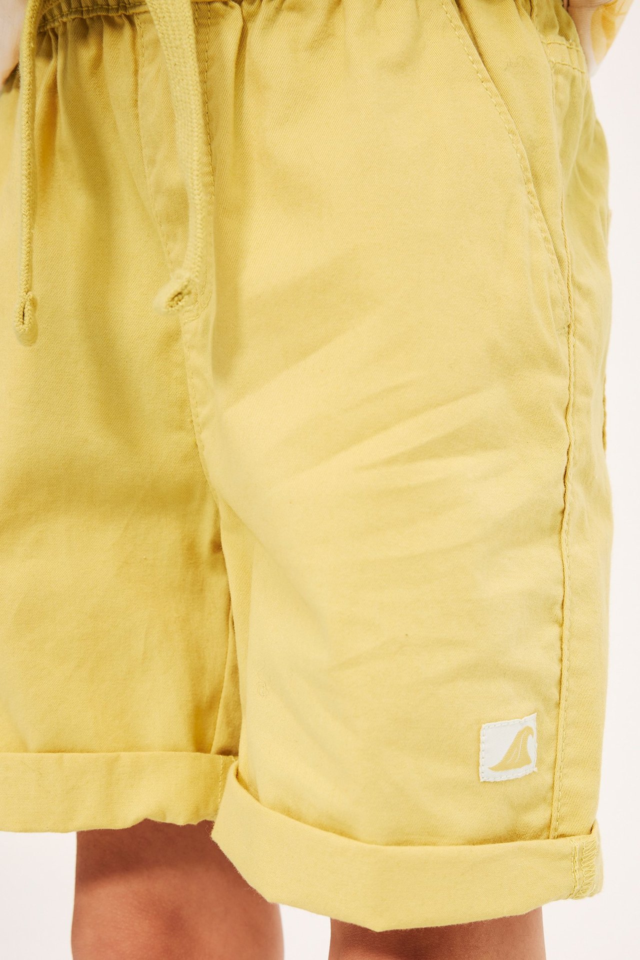 Zbliżenie na żółte bawełniane szorty dziecięce z elastyczną talią, sznurkiem i podwiniętymi nogawkami.