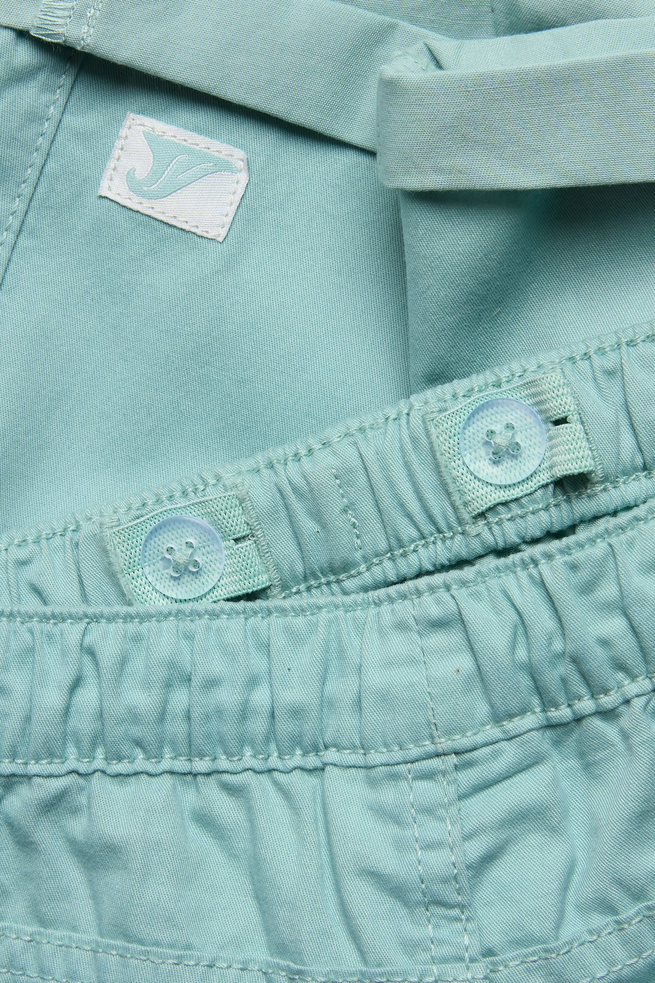 Nærbilde av lysegrønne bomullsshorts for barn med elastisk linning og justerbare knapper.