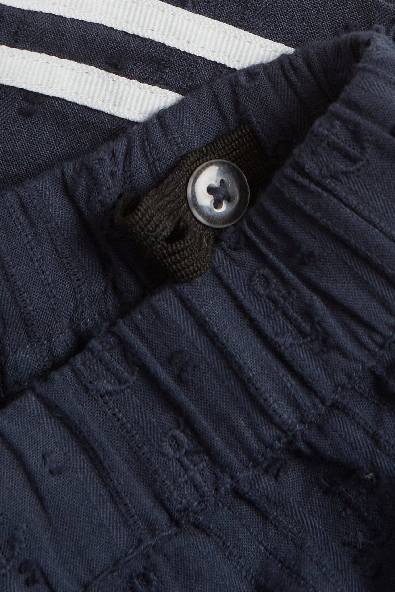 Närbild av mörkblå vävda bomullsshorts med justerbar midja och knapp, stylade med randig skjorta.