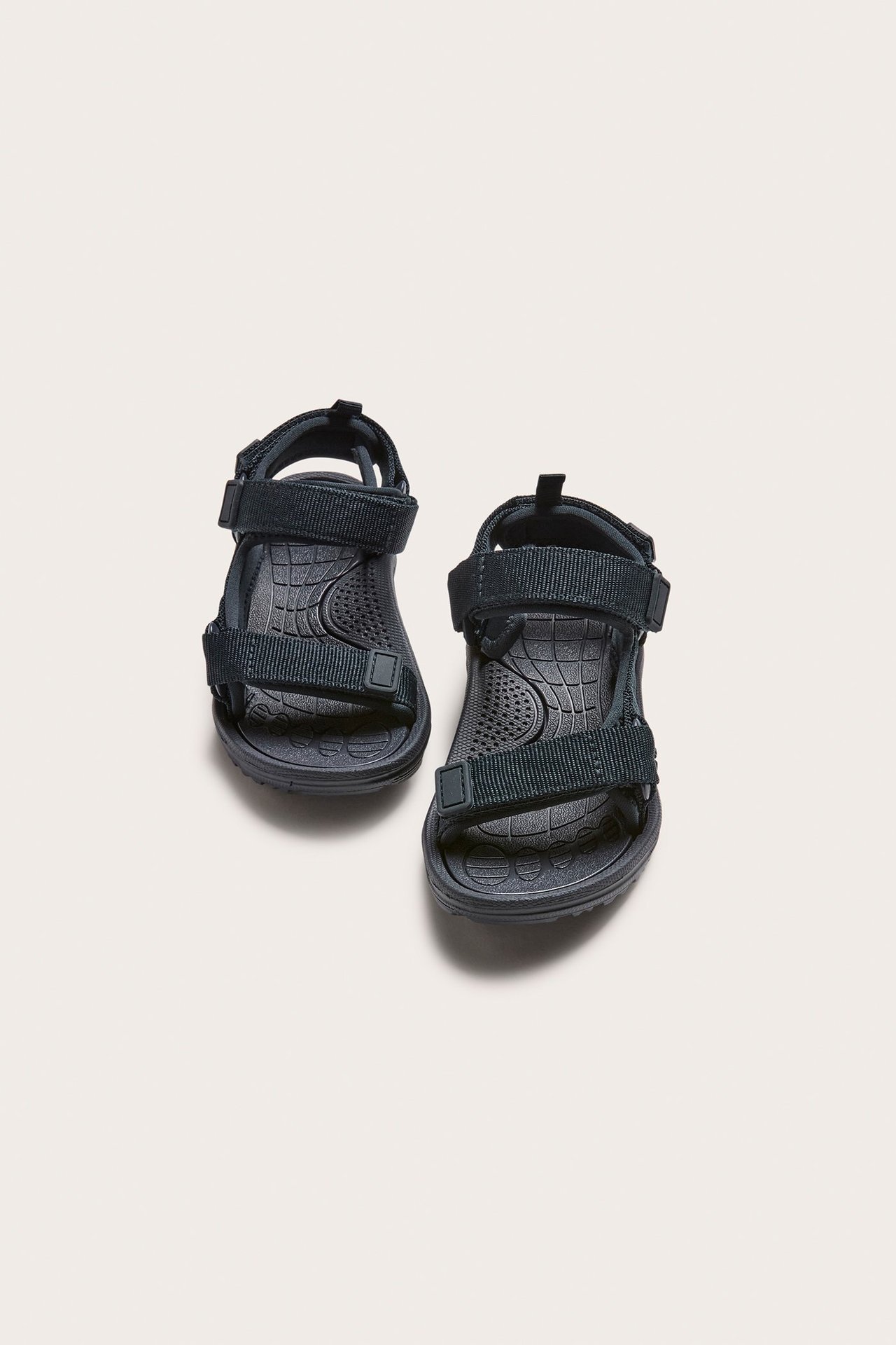 Uppifrån, ett par mörkblå barnsandaler med justerbara kardborreband i polyester.