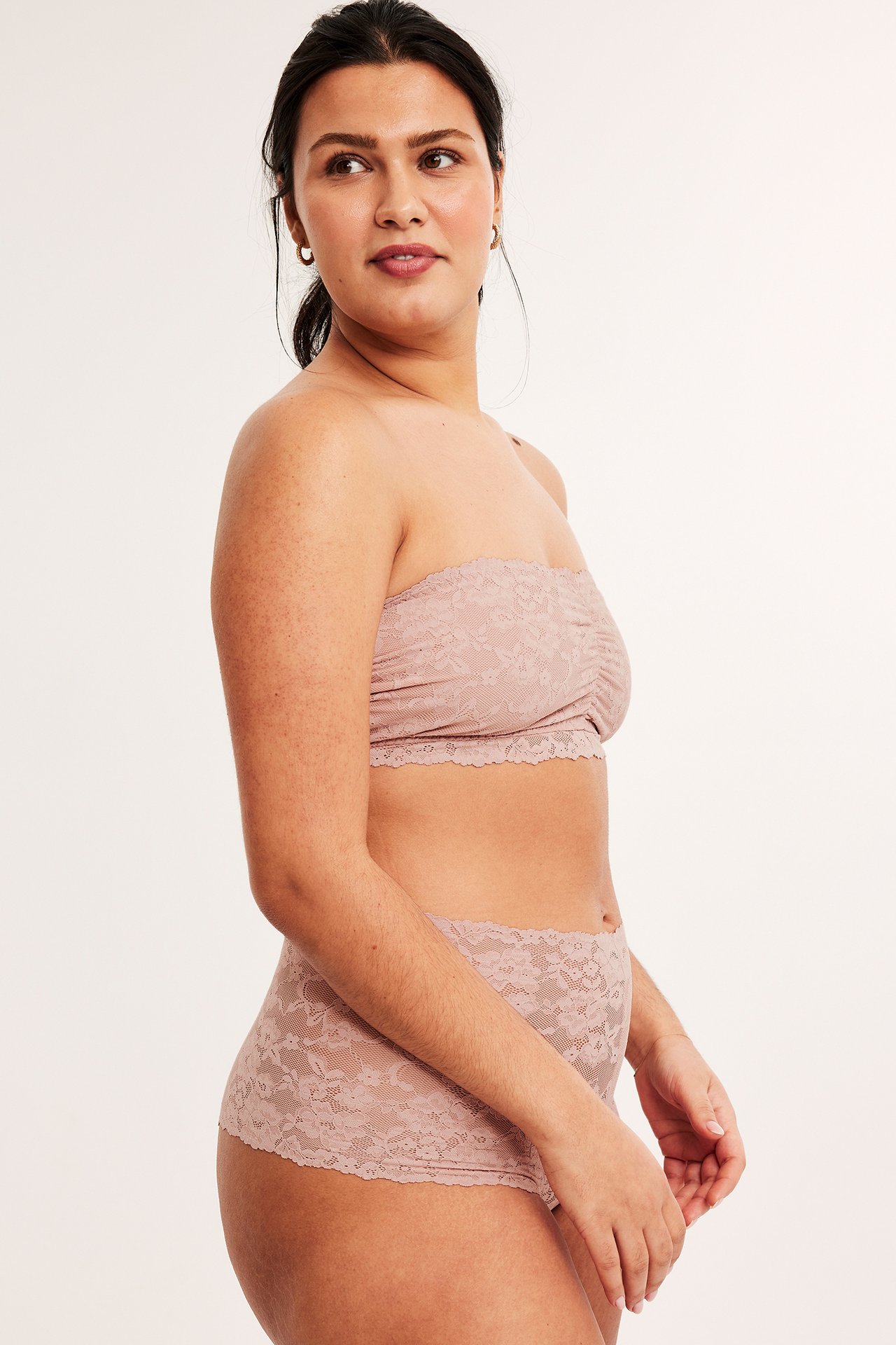 Sidebilde av en kvinne i lyserosa blonde cheeky truser og matchende blonde bandeau-bh.