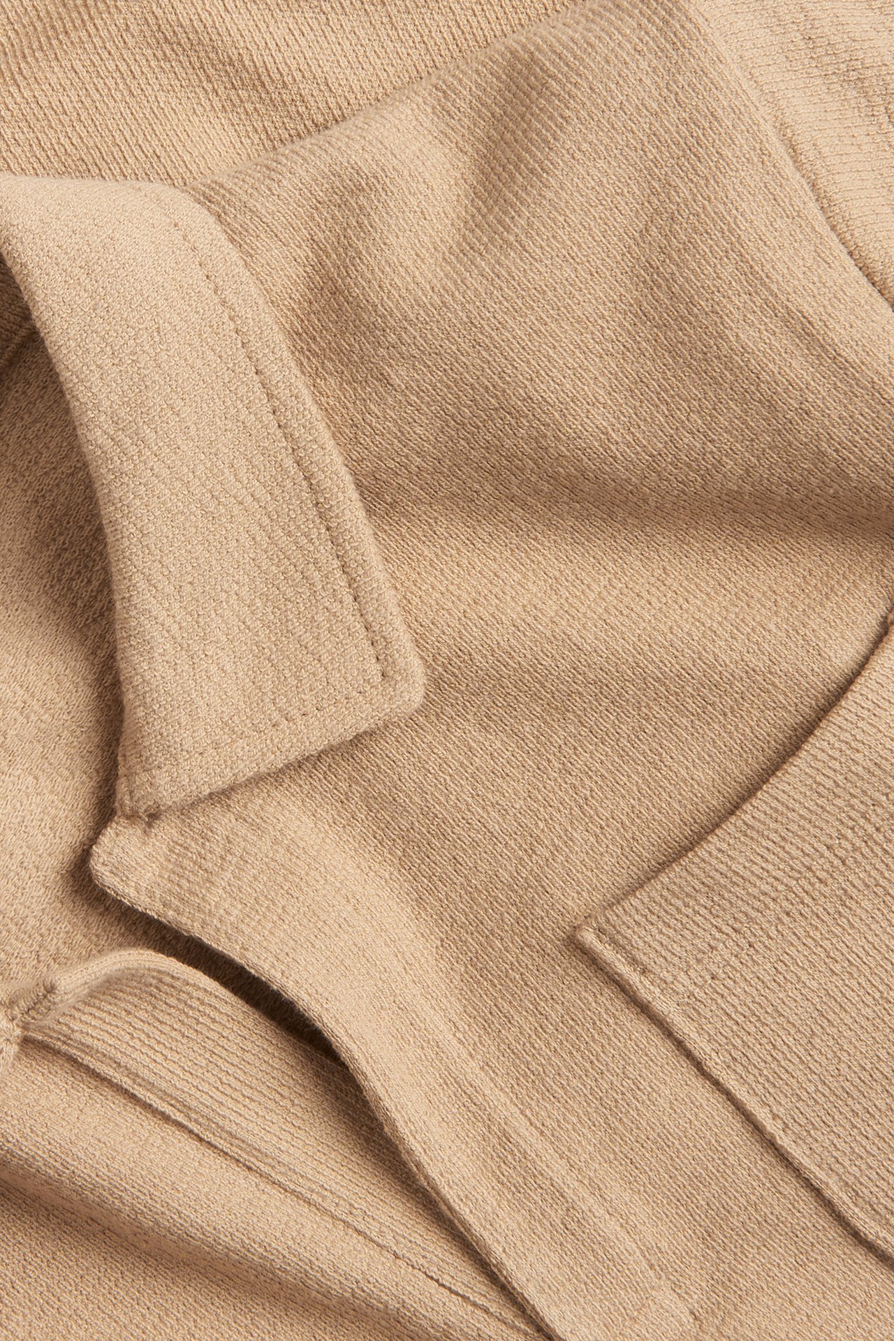 Närbild av en beige texturerad pikétröja i bomull med krage och bröstficka.