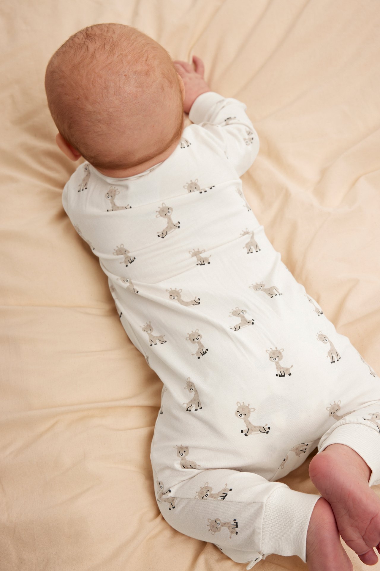 Uppifrån-vy av en baby i en offwhite bomullsromper med brunt giraffmönster.
