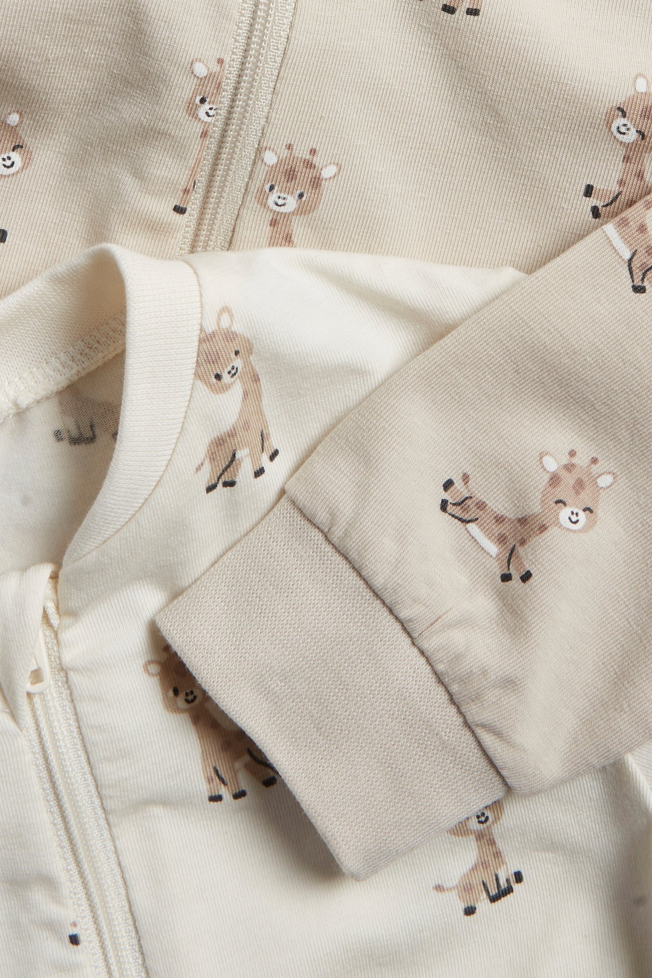 Närbild av två offwhite och ljusbeige baby-pyjamasar med giraffmönster och tvåvägsdragkedja.