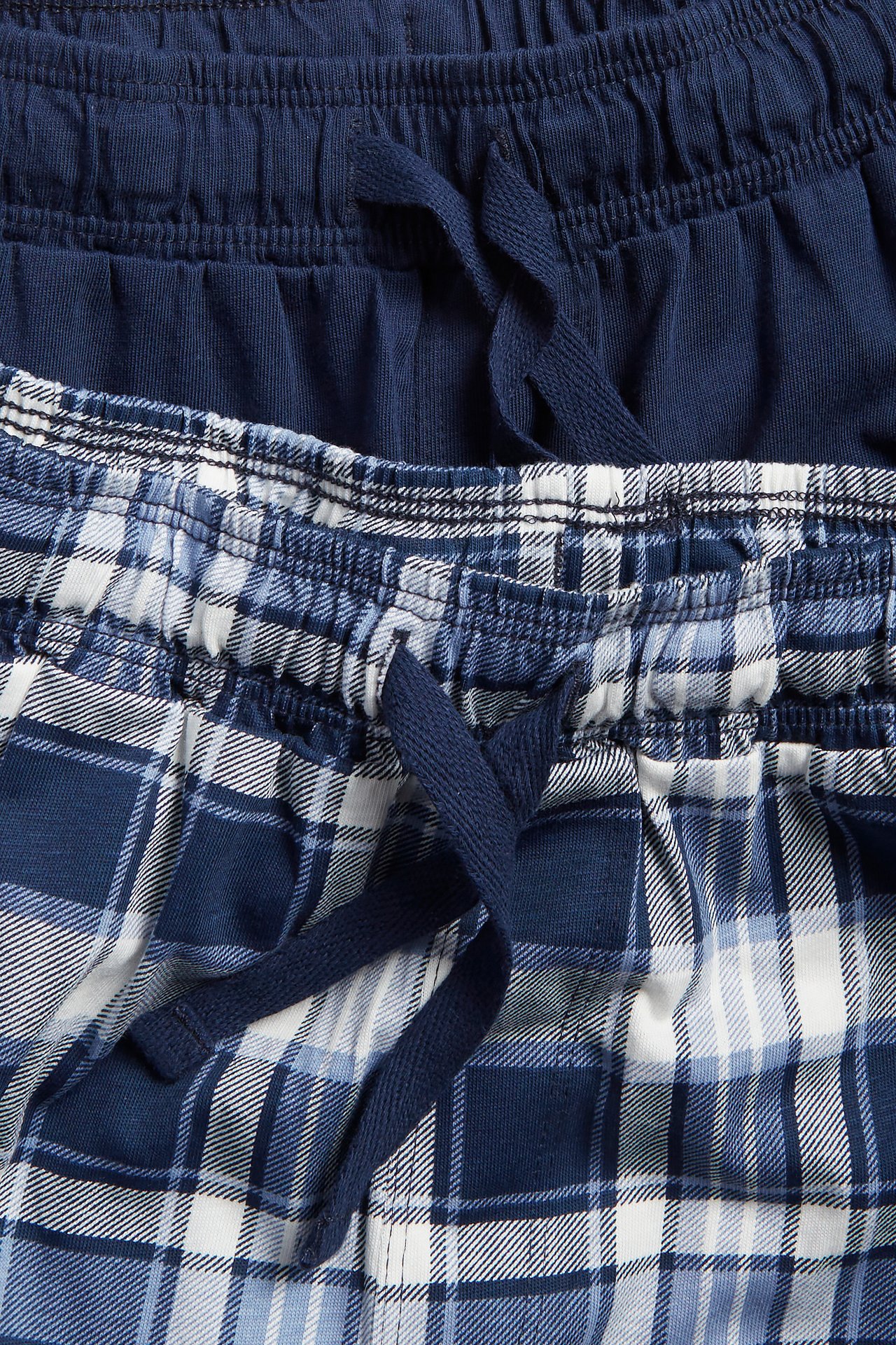 Lähikuva kahdesta parista lasten pyjamashortseja: yhdet tummansiniset ruudulliset, yhdet yksiväriset tummansiniset, molemmissa kiristysnyörit.