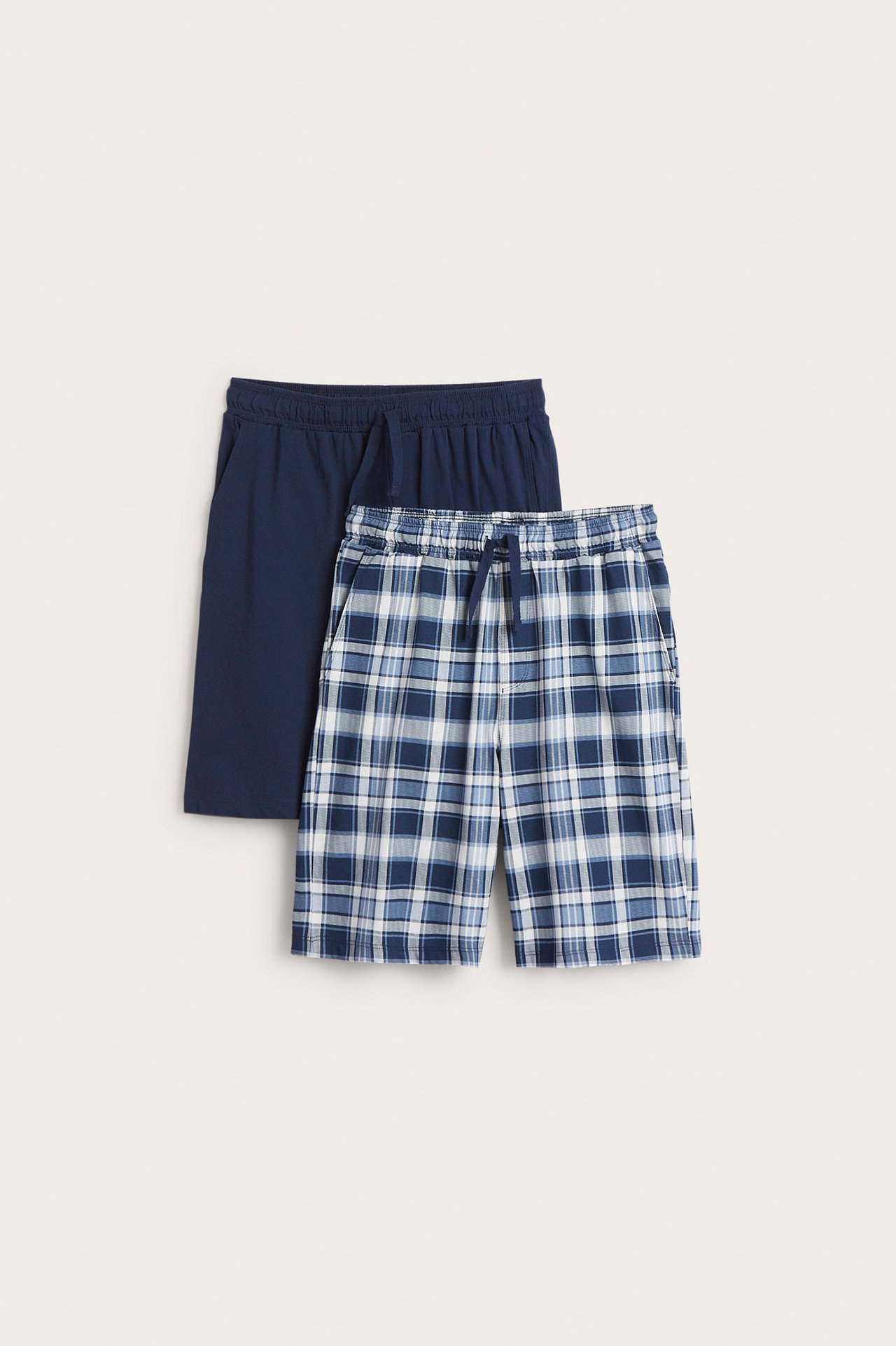 Edestä: Kahdet lasten puuvillapyjamashortsit; yhdet sinivalkoruudulliset, yhdet yksiväriset tummansiniset.