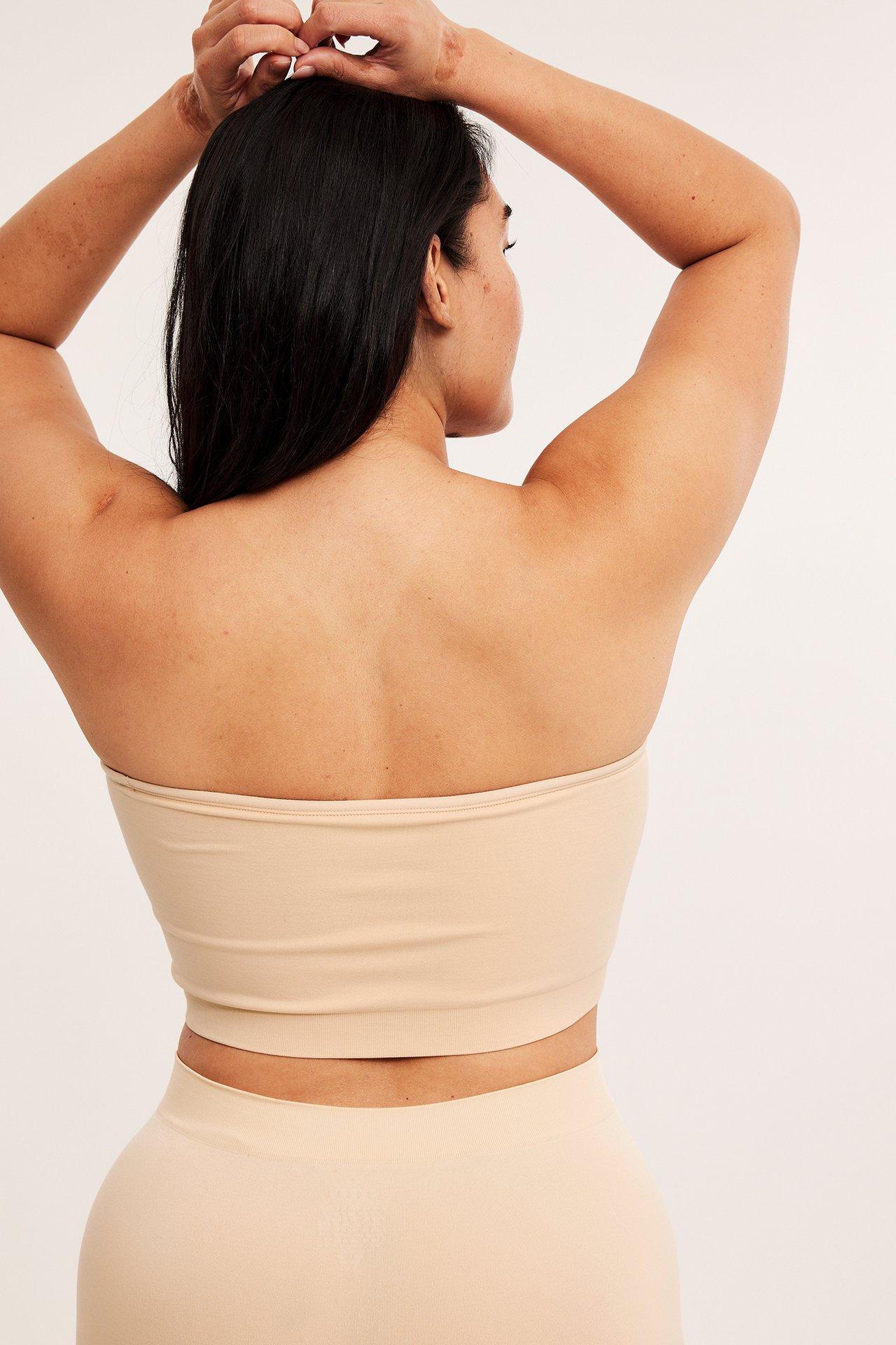 Naisen selkäkuva, yllään saumaton beige bandeau-rintaliivi ja yhteensopiva saumaton alaosa.