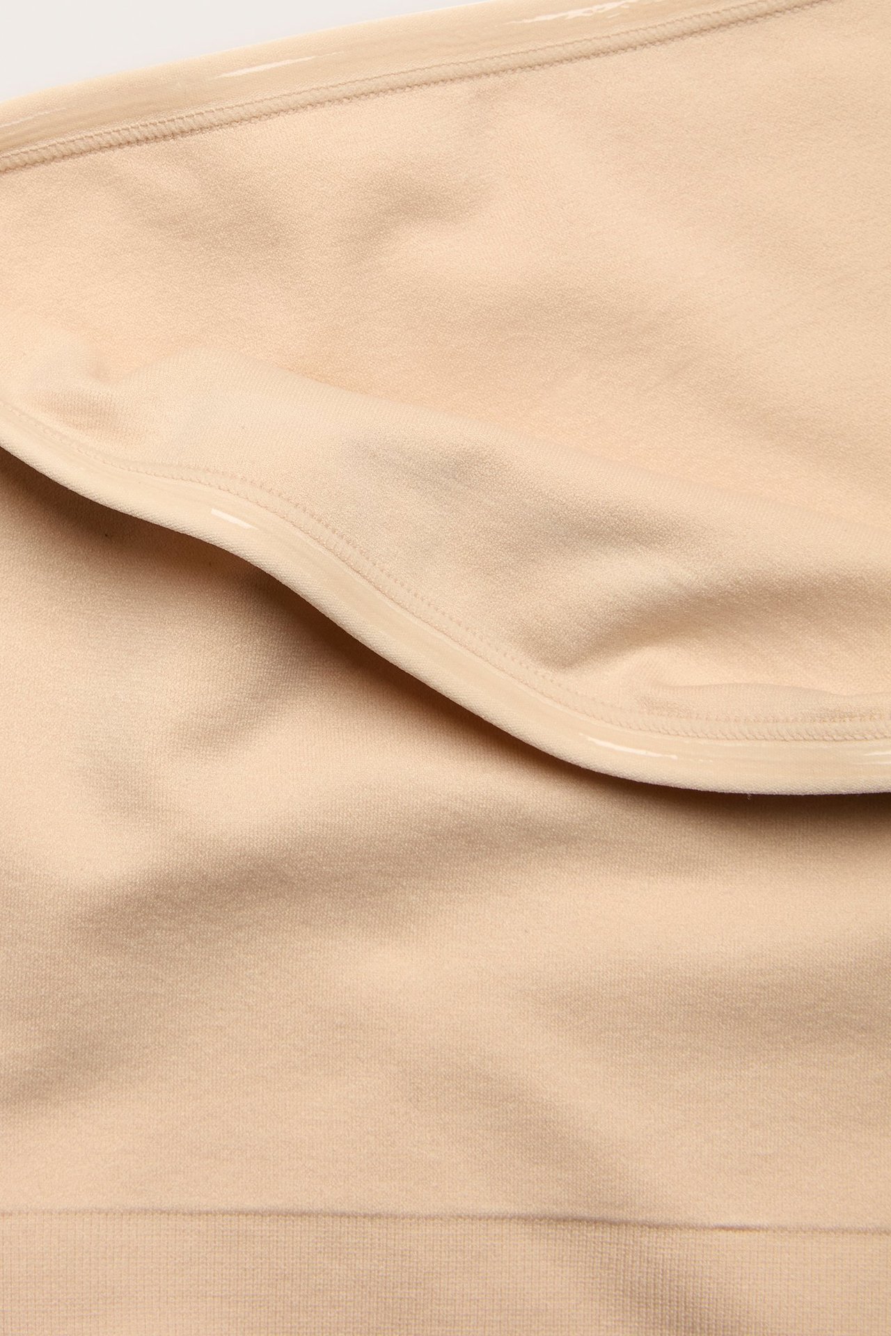 Zbliżenie beżowego, bezszwowego biustonosza bandeau z silikonową taśmą na wewnętrznej górnej krawędzi.