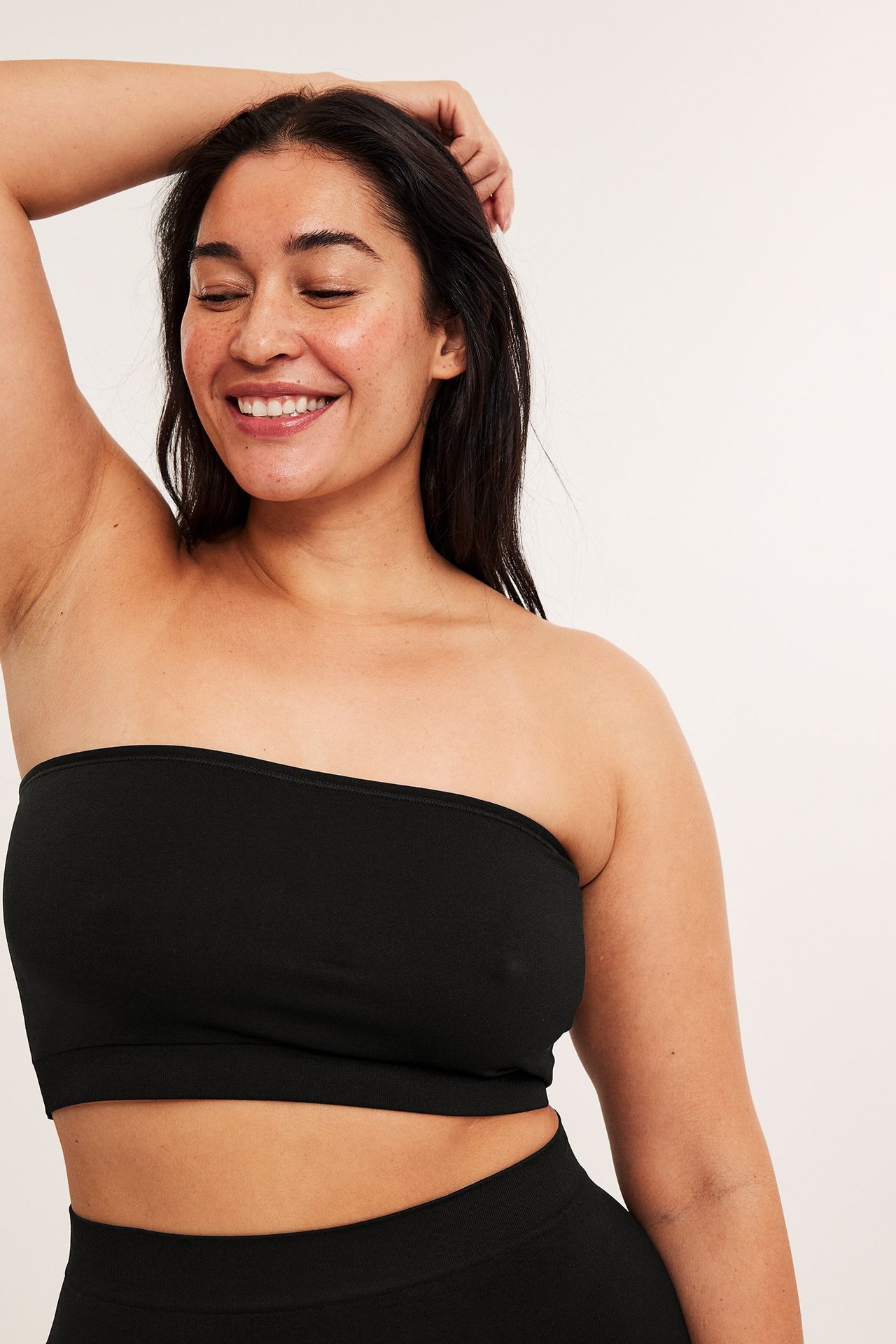 Närbild framifrån på en kvinna i en svart sömlös bandeau-bh och matchande svarta sömlösa trosor.