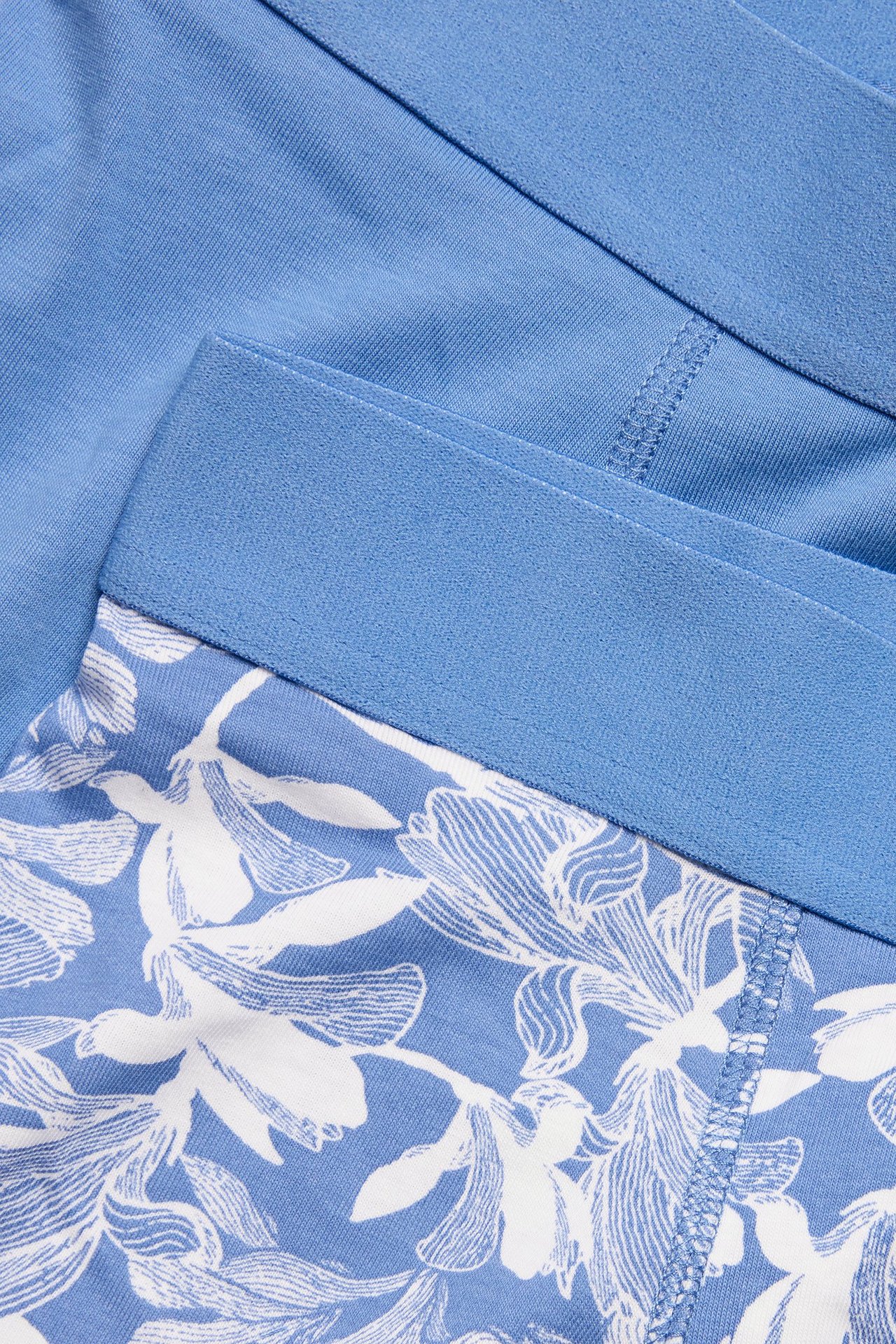 Närbild av herrboxerkalsonger i bomull/elastan, en ljusblå och en mönstrad med vita blommor.