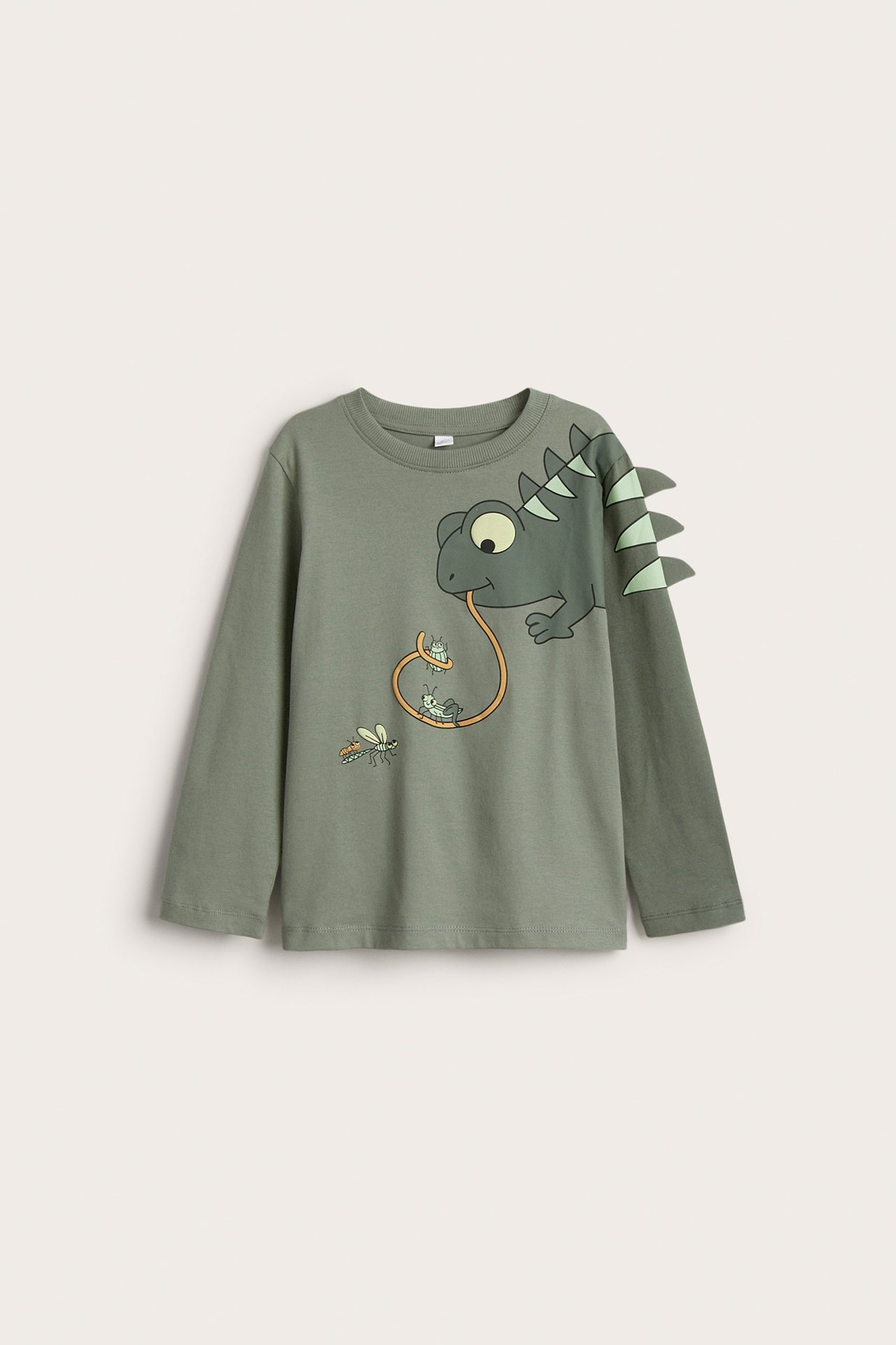 Frontvy av en grön långärmad T-shirt i bomull för barn med ödletryck och taggapplikationer.