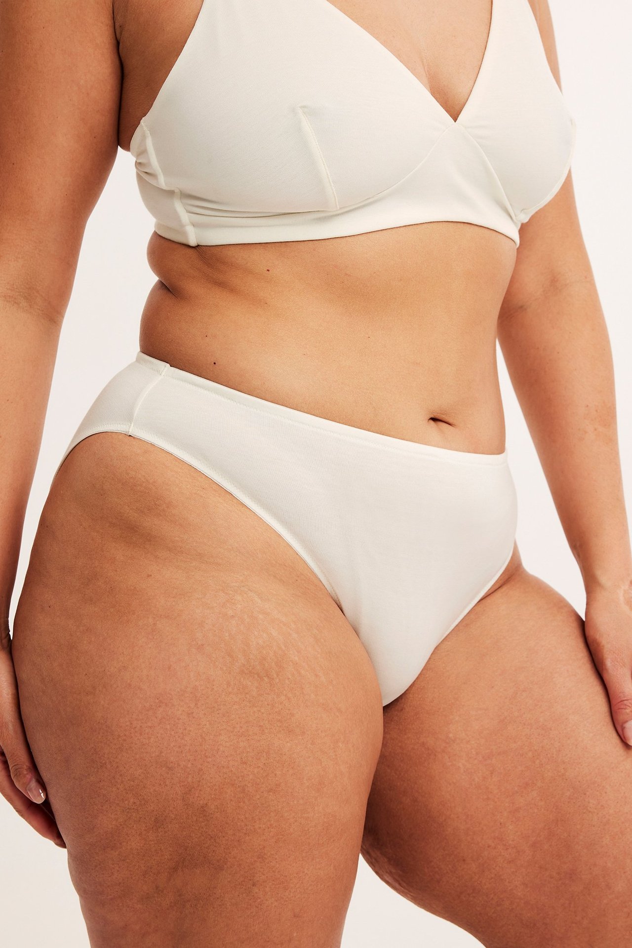 Widok z boku na kobietę w białych lyocellowych figach brazilian i pasującym białym biustonoszu.