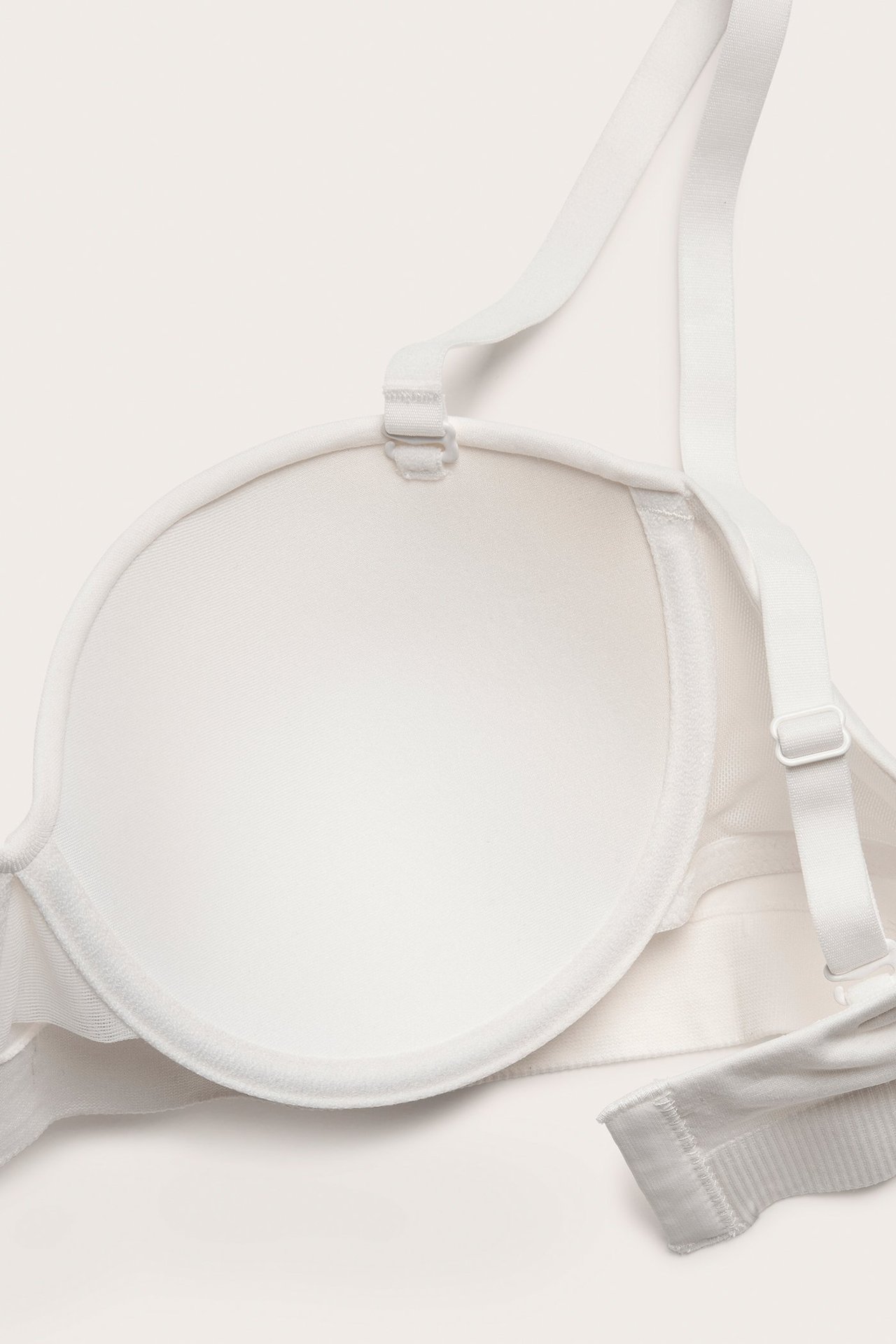 Zbliżenie białego, bezszwowego biustonosza typu balconette z formowanymi miseczkami i odpinanymi, regulowanymi ramiączkami.