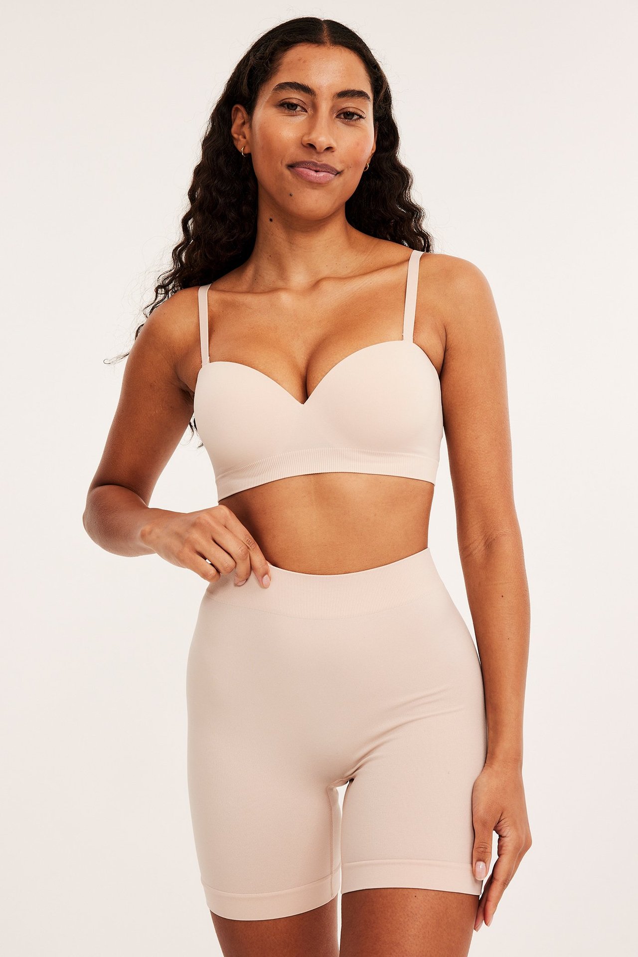 Forfra, kvinne i lys rosa sømløse high-waist shorts og matchende stroppeløs BH.