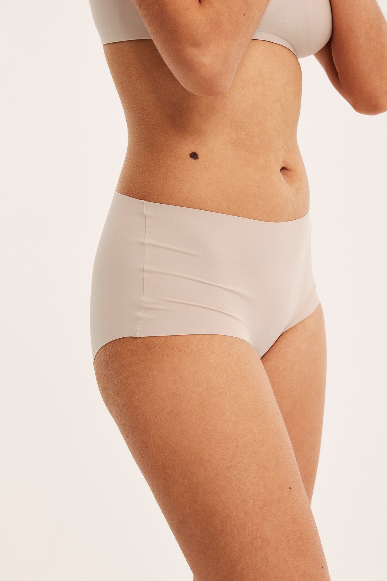 Sivukuva naisesta yllään vaaleanpunaiset saumattomat hipster-alushousut ja yhteensopivat rintaliivit.