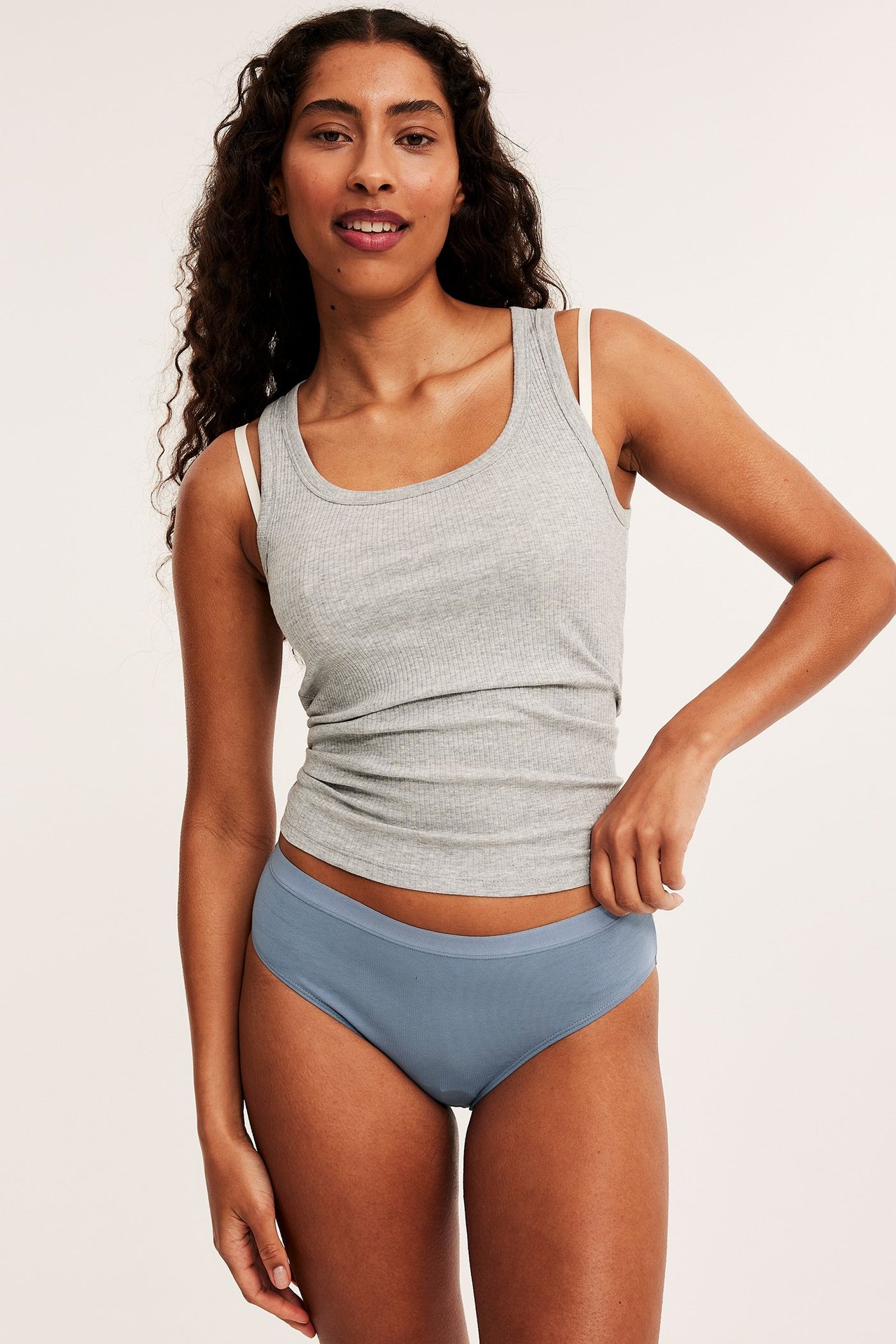 Forfra, kvinne i ensfargede blå truser, grå ribbet singlet og hvite BH-stropper.