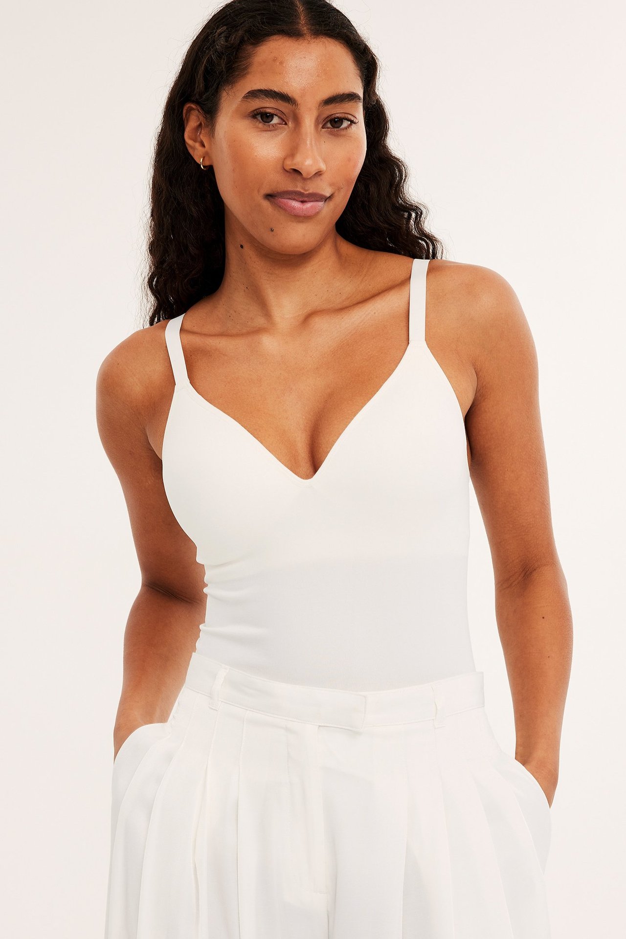 Forfra: kvinne i hvit sømløs singlet med innebygd BH og hvite vide bukser.