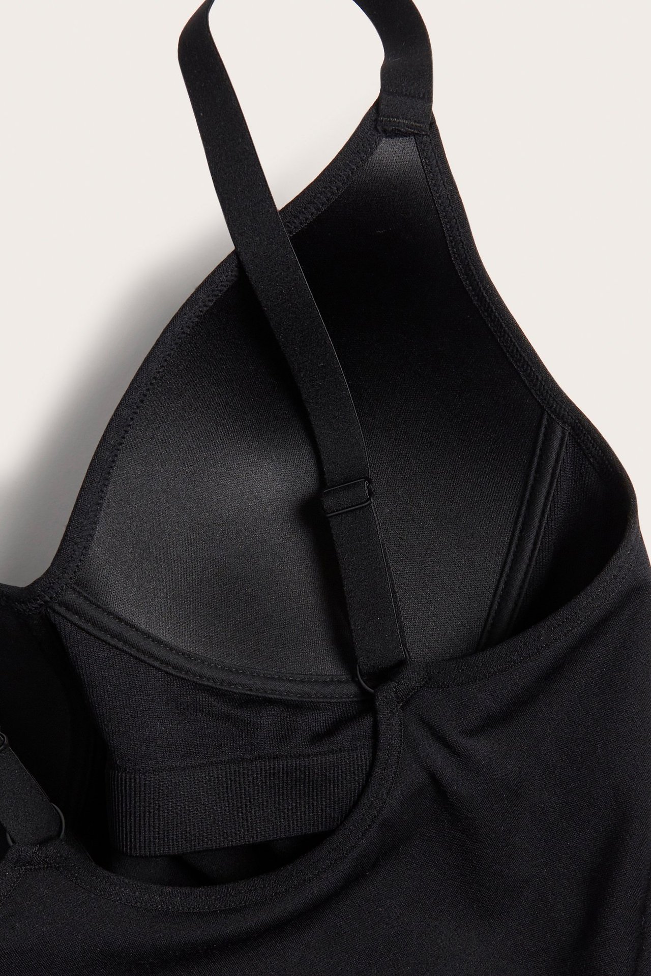 Zbliżenie czarnego, bezszwowego topu z wbudowanym biustonoszem, formowaną miseczką i regulowanym ramiączkiem.