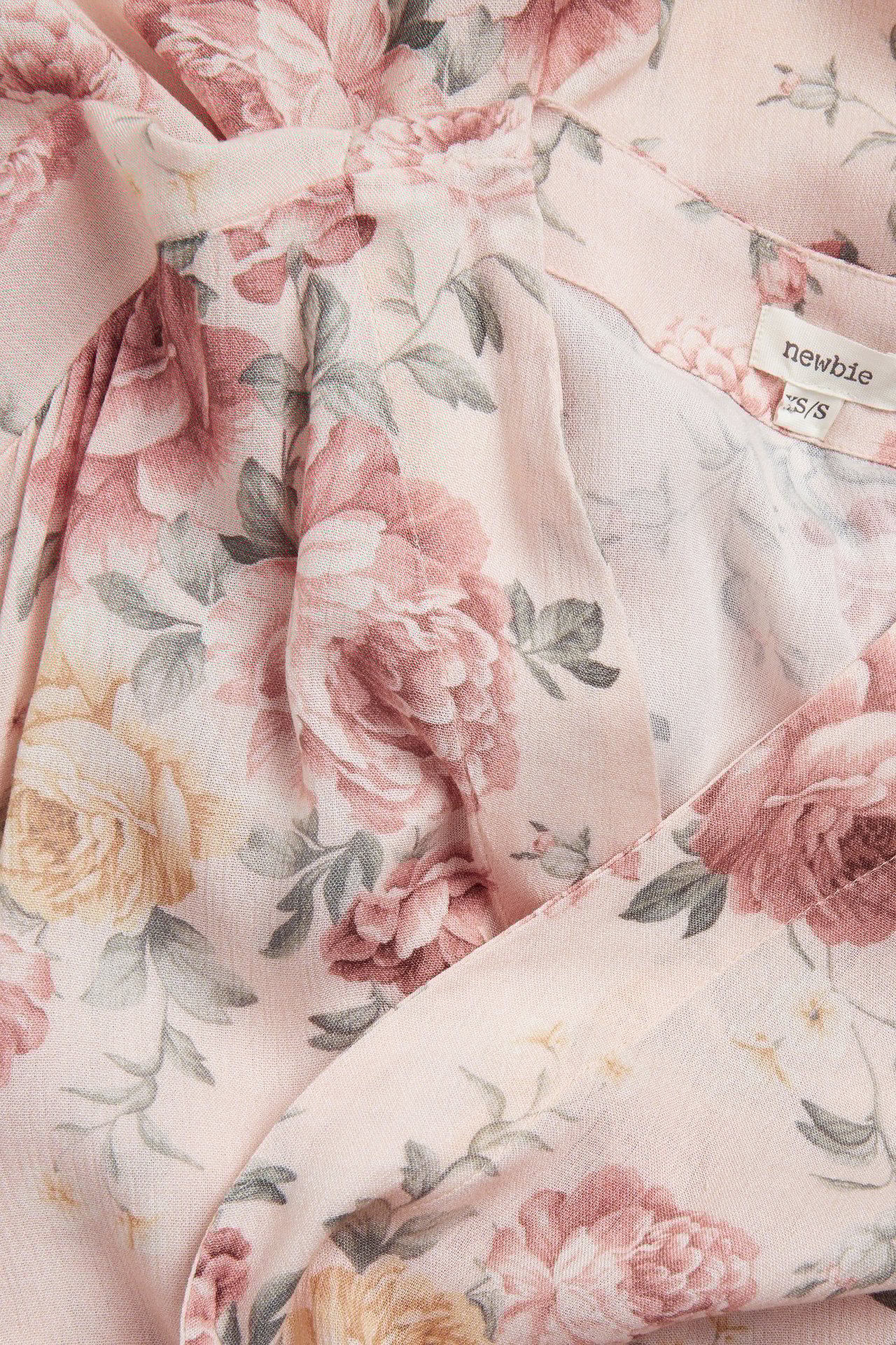 Zbliżenie różowego kimona z wiskozy w kwiatowy wzór, z widoczną metką Newbie.