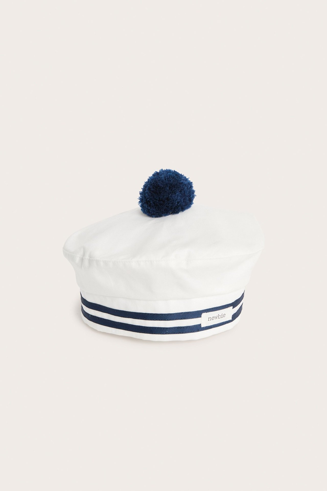 Widok z przodu: kremowy bawełniany beret dla niemowląt/dzieci z granatowymi paskami i pomponem.