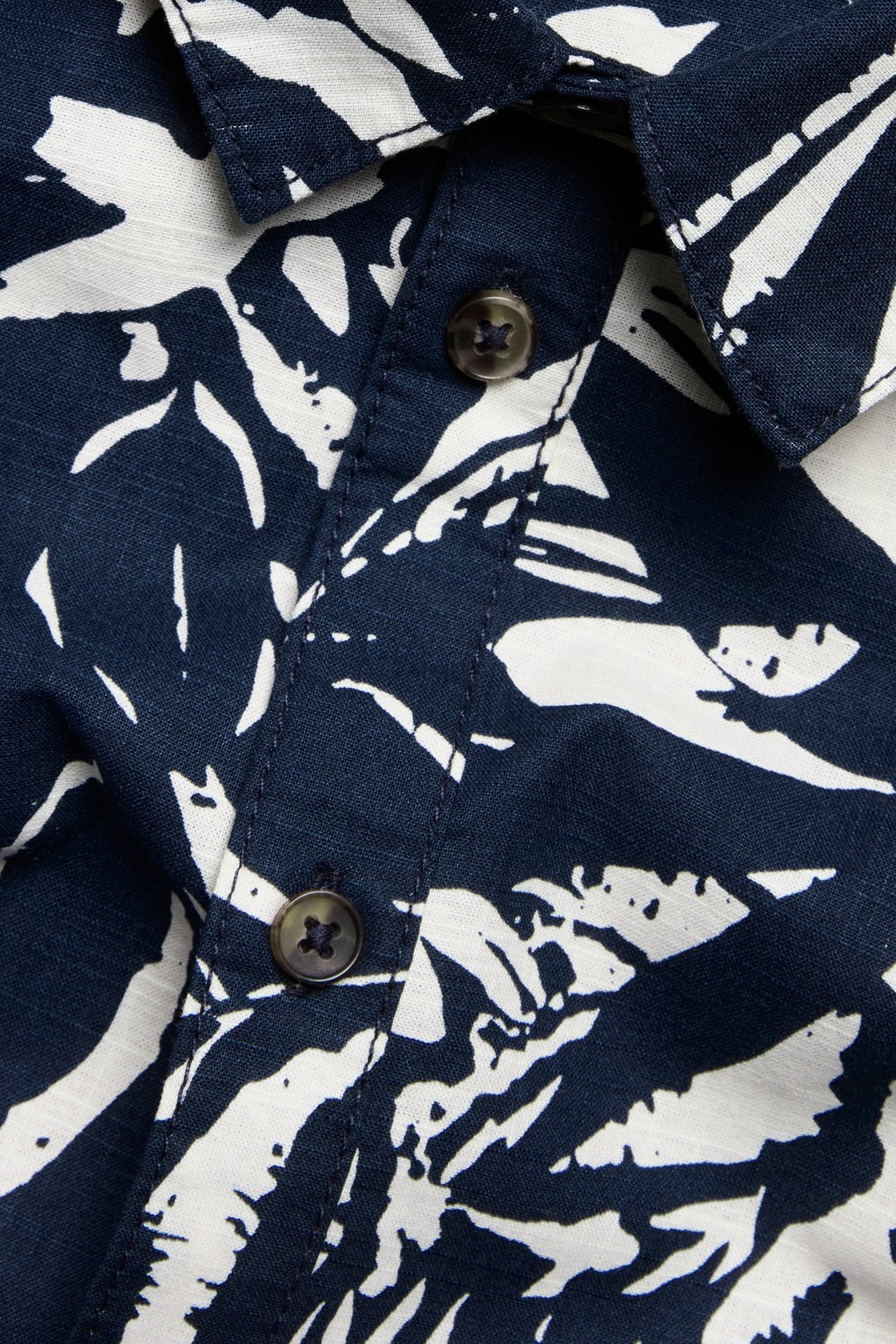 Zbliżenie na granatową i białą wzorzystą bawełnianą koszulę z krótkim rękawem, zapinaną na guziki.
