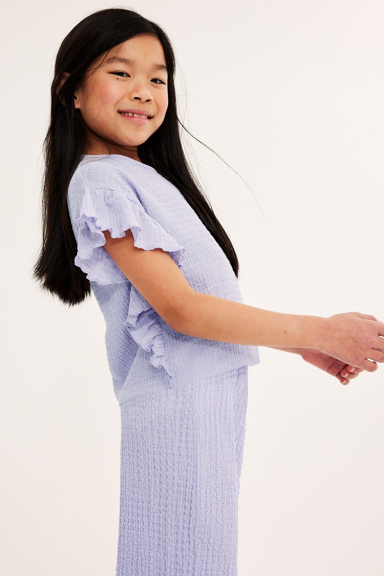 Widok z boku dziecka w liliowym teksturowanym topie z falbankami i pasujących teksturowanych spodniach.