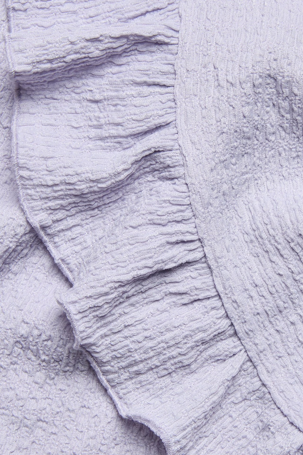 Zbliżenie na liliowy, teksturowany top z falbankami i marszczonymi brzegami.