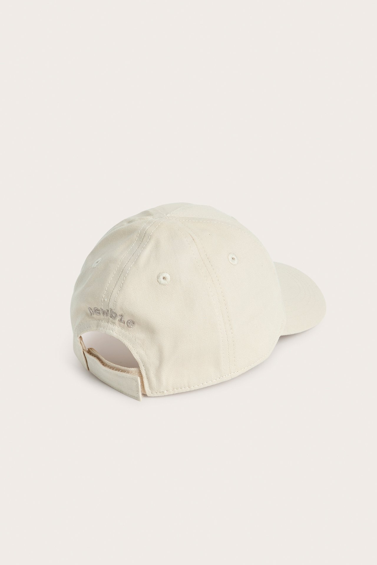 Bakifrån av en beige barnkeps med enfärgat mönster och 'Newbie' broderat baktill.