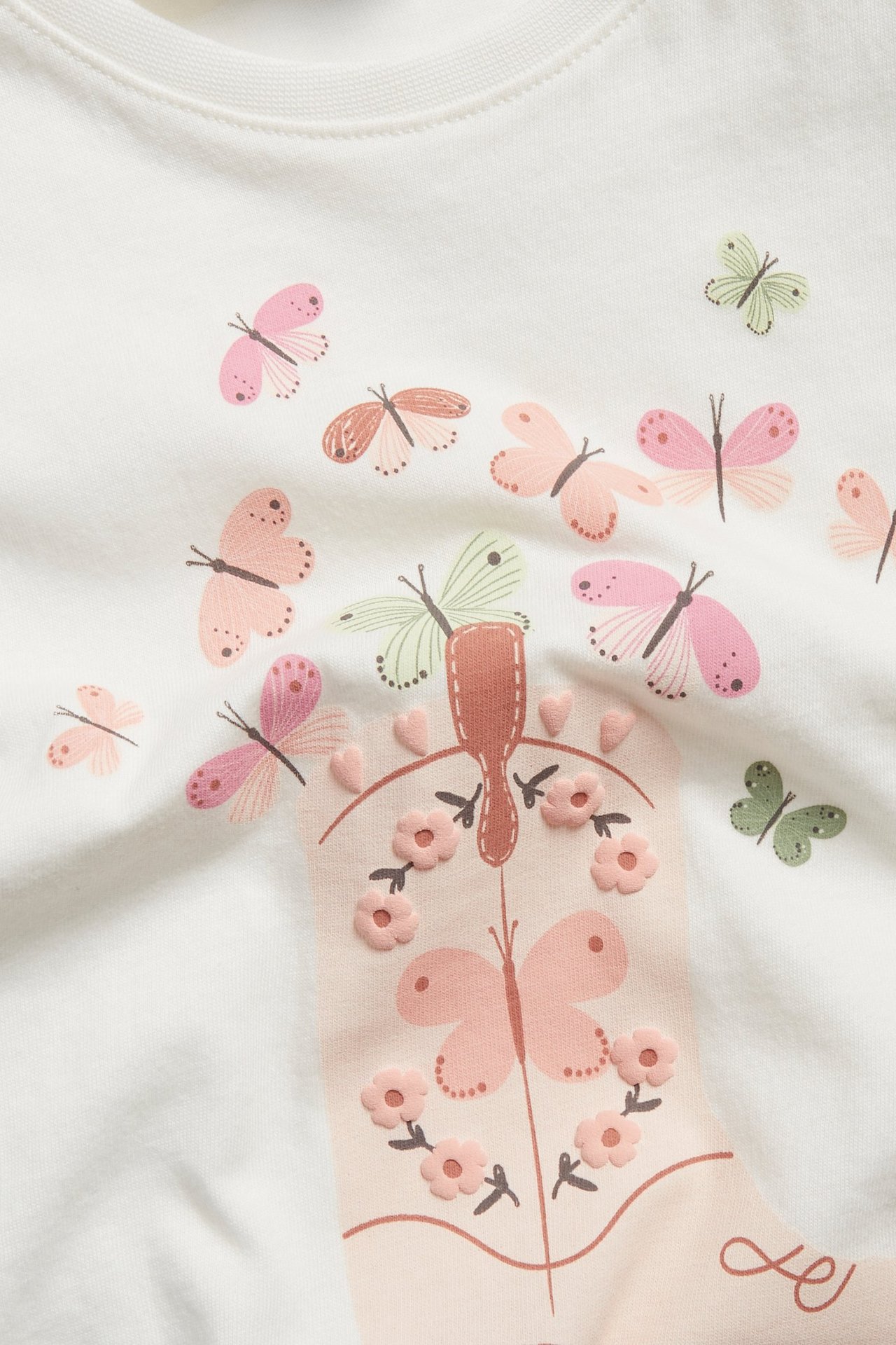 Zbliżenie na ecru bawełniany top z kolorowym nadrukiem motyli i wytłoczonych kwiatów.