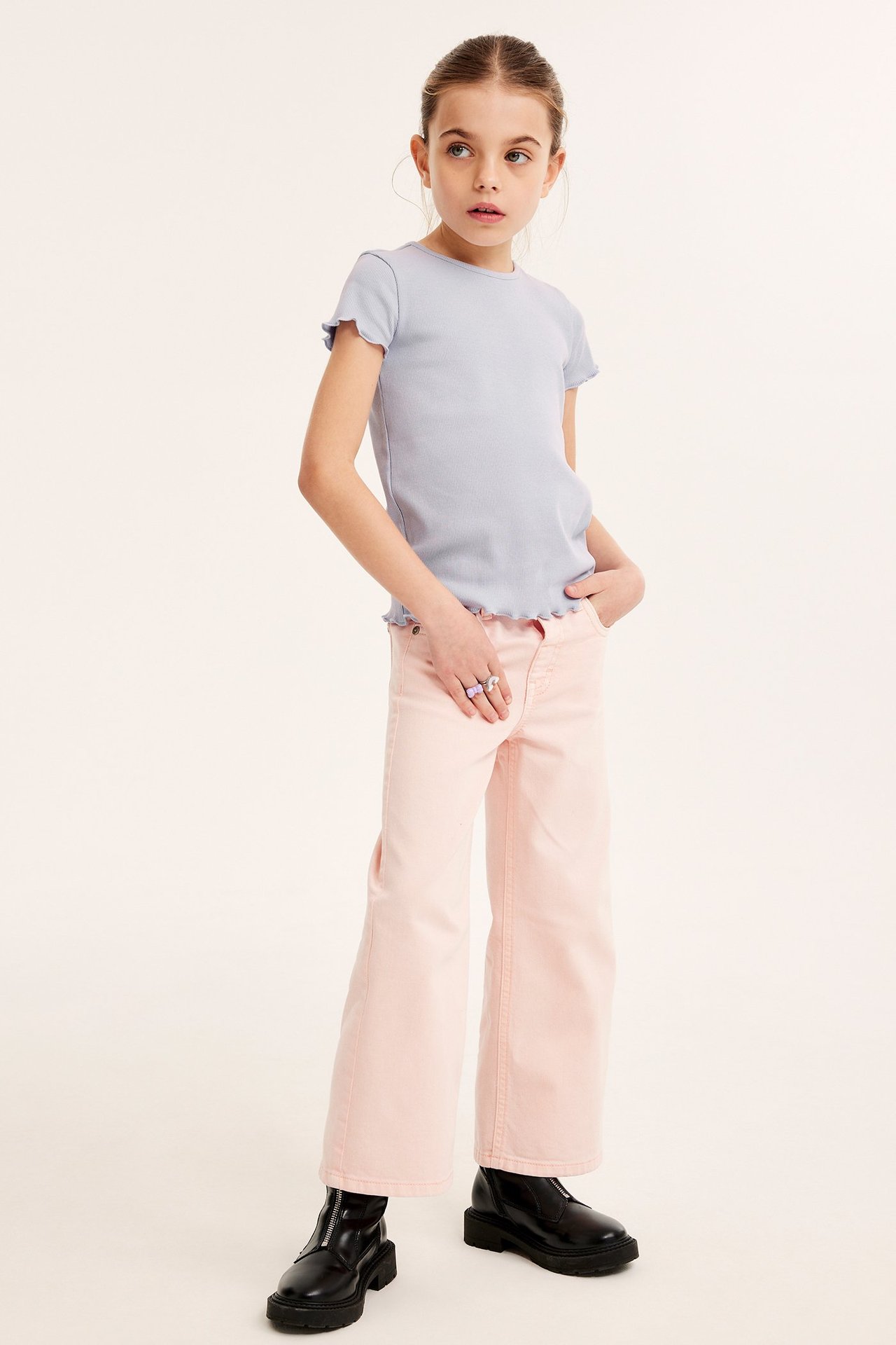 Widok z przodu: Dziecko w liliowym prążkowanym topie babylock, różowych spodniach, czarnych butach.
