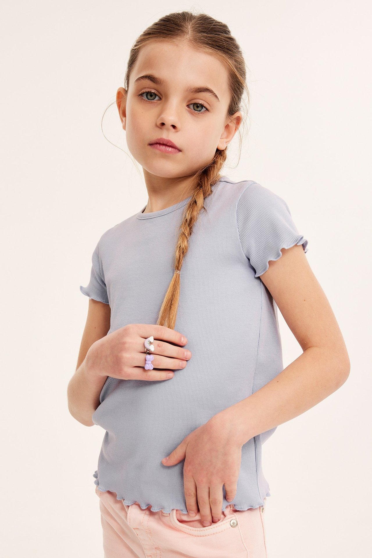 Dziecko w liliowym prążkowanym topie z falbankami, jasnoróżowych spodniach i dwoma pierścionkami.