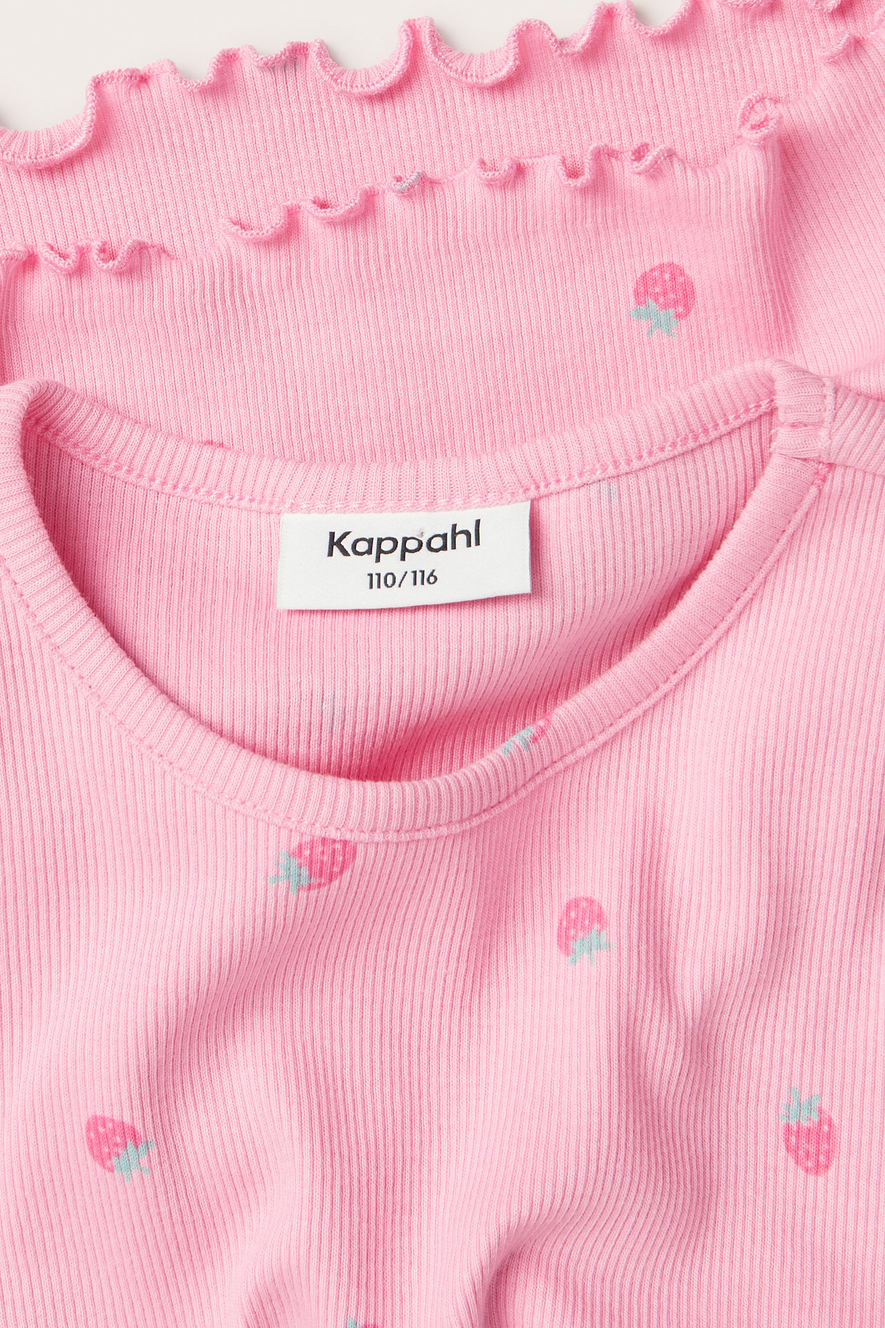 Nærbilde av to rosa ribbestrikkede barnetopper med jordbærmønster; en rund hals, en med babylock-kant.
