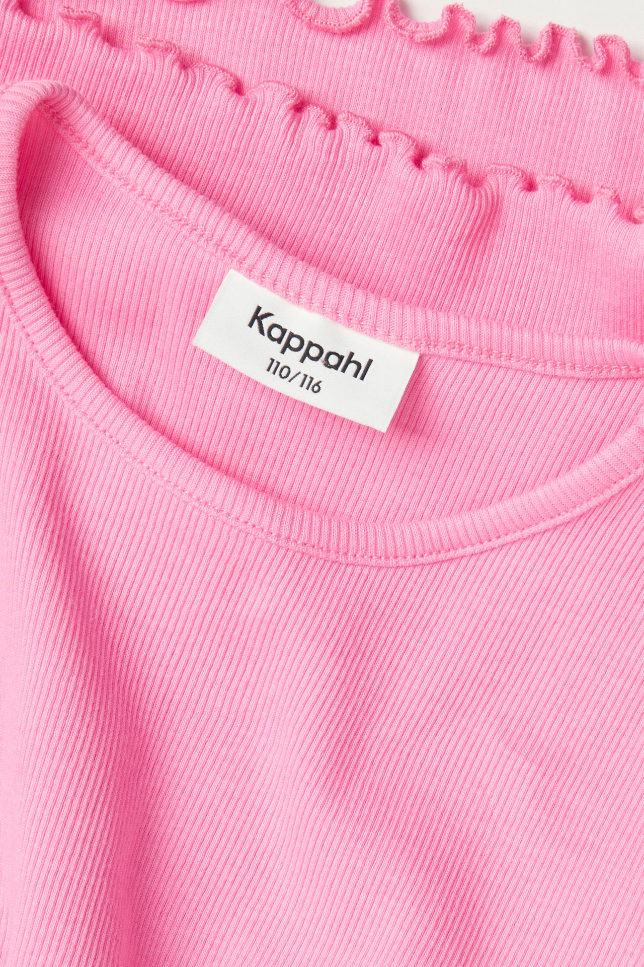 Närbild av en rosa ribbad kortärmad barntopp med rund halsringning och babylockkant.