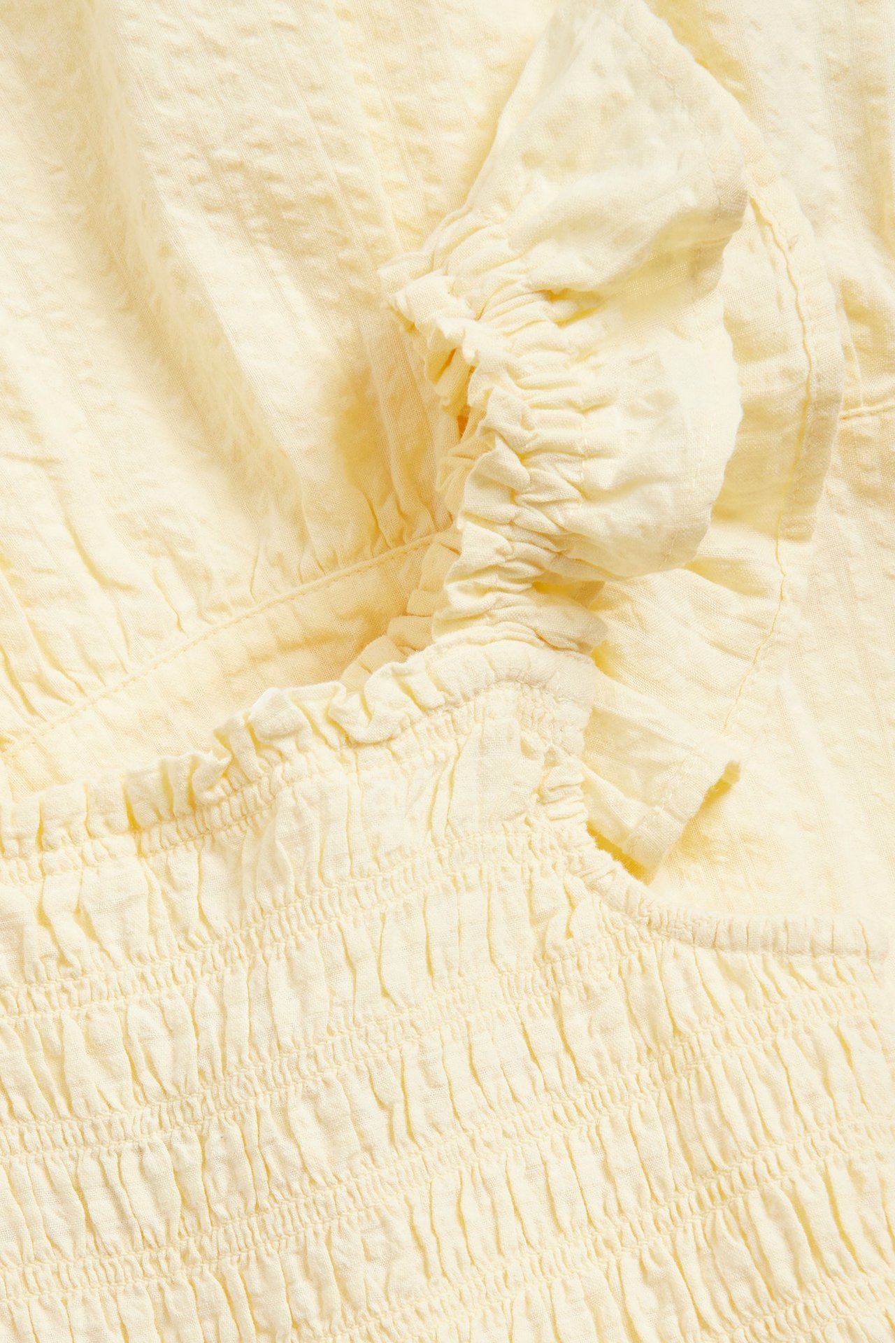 Zbliżenie jasnobeżowej sukienki z bawełnianego seersuckeru ze smockowanym gorsetem i falbankami.