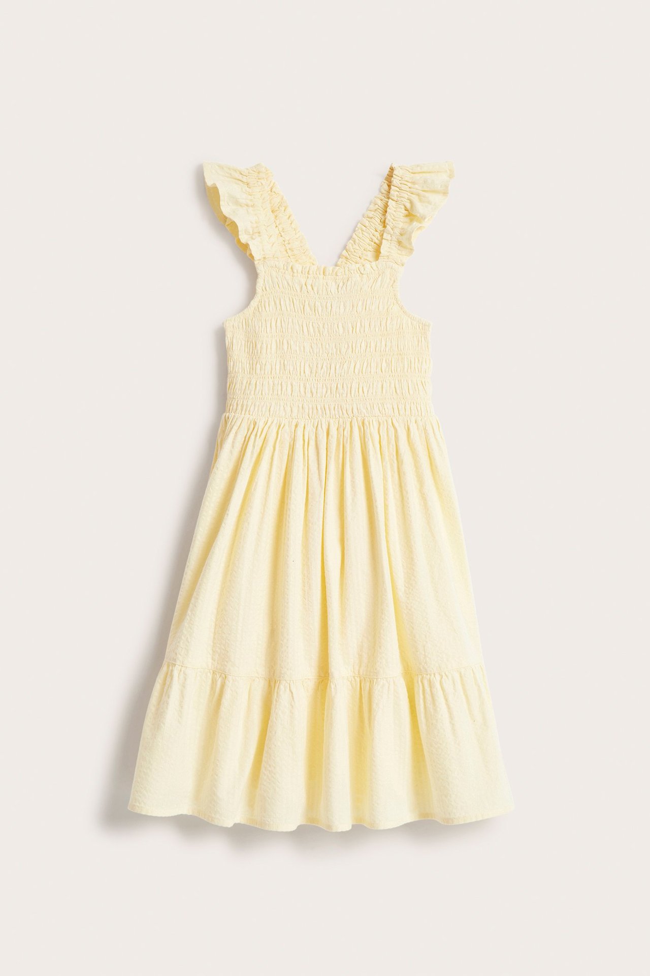 Widok z przodu: Jasnobeżowa sukienka dziecięca z bawełny seersucker, ze smockowanym gorsetem i falbankami.