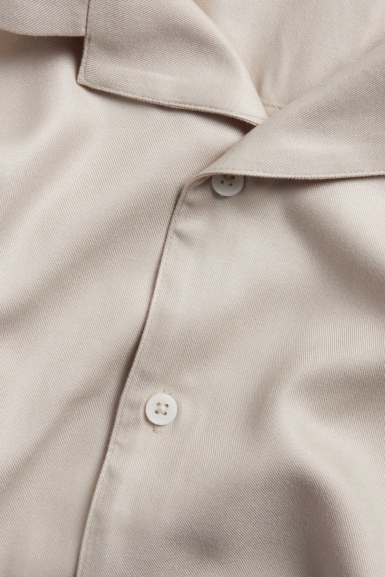 Zbliżenie na męską jasnobeżową koszulę z krótkim rękawem z wiskozy, z kołnierzykiem i białymi guzikami.