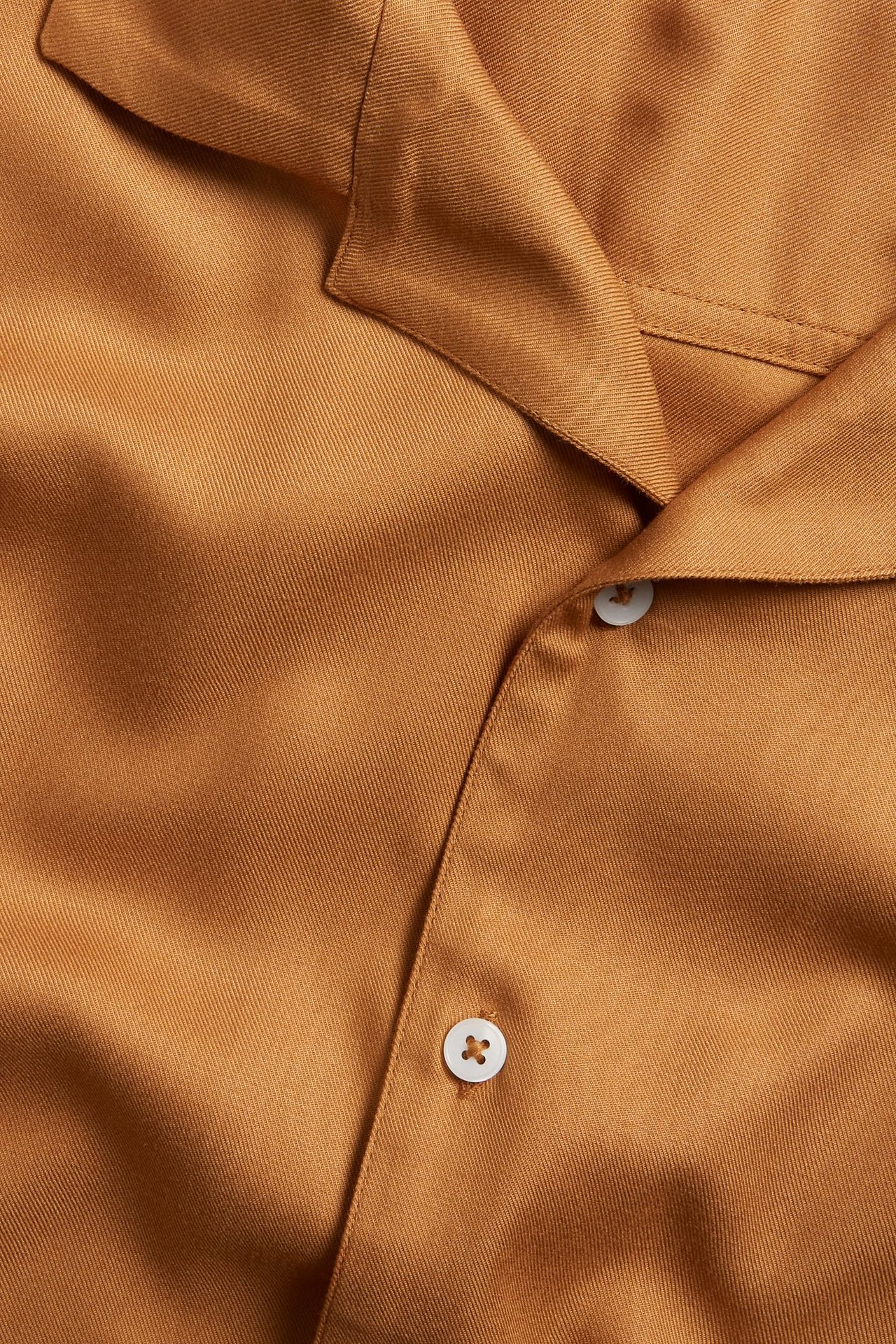 Lähikuva miesten ruskeasta viskoosipaidasta, jossa on lyhyet hihat, camp-kaulus ja valkoiset napit.