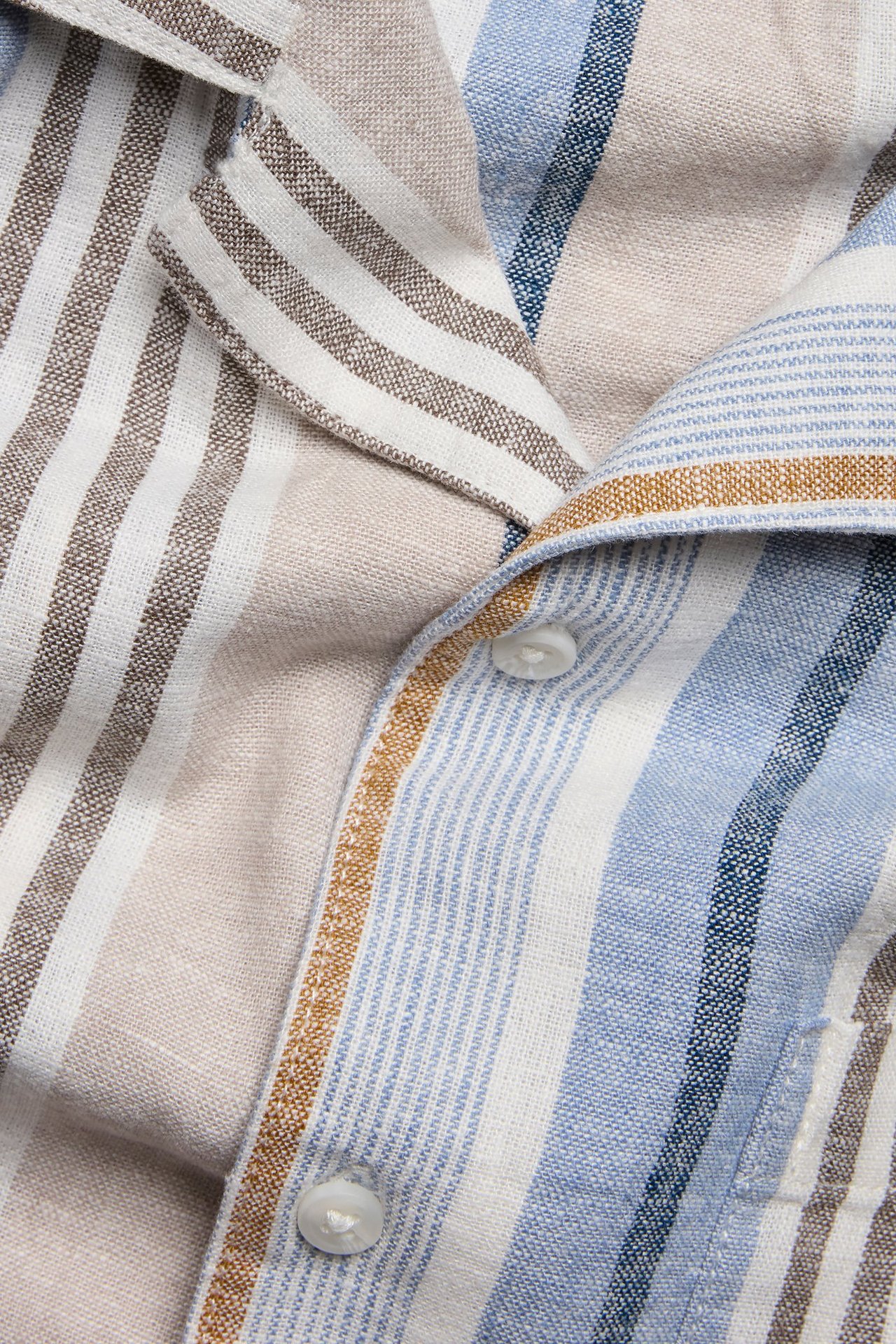 Zbliżenie męskiej koszuli w paski z mieszanki lnu, z niebieskimi, białymi i brązowymi paskami, z białymi guzikami.