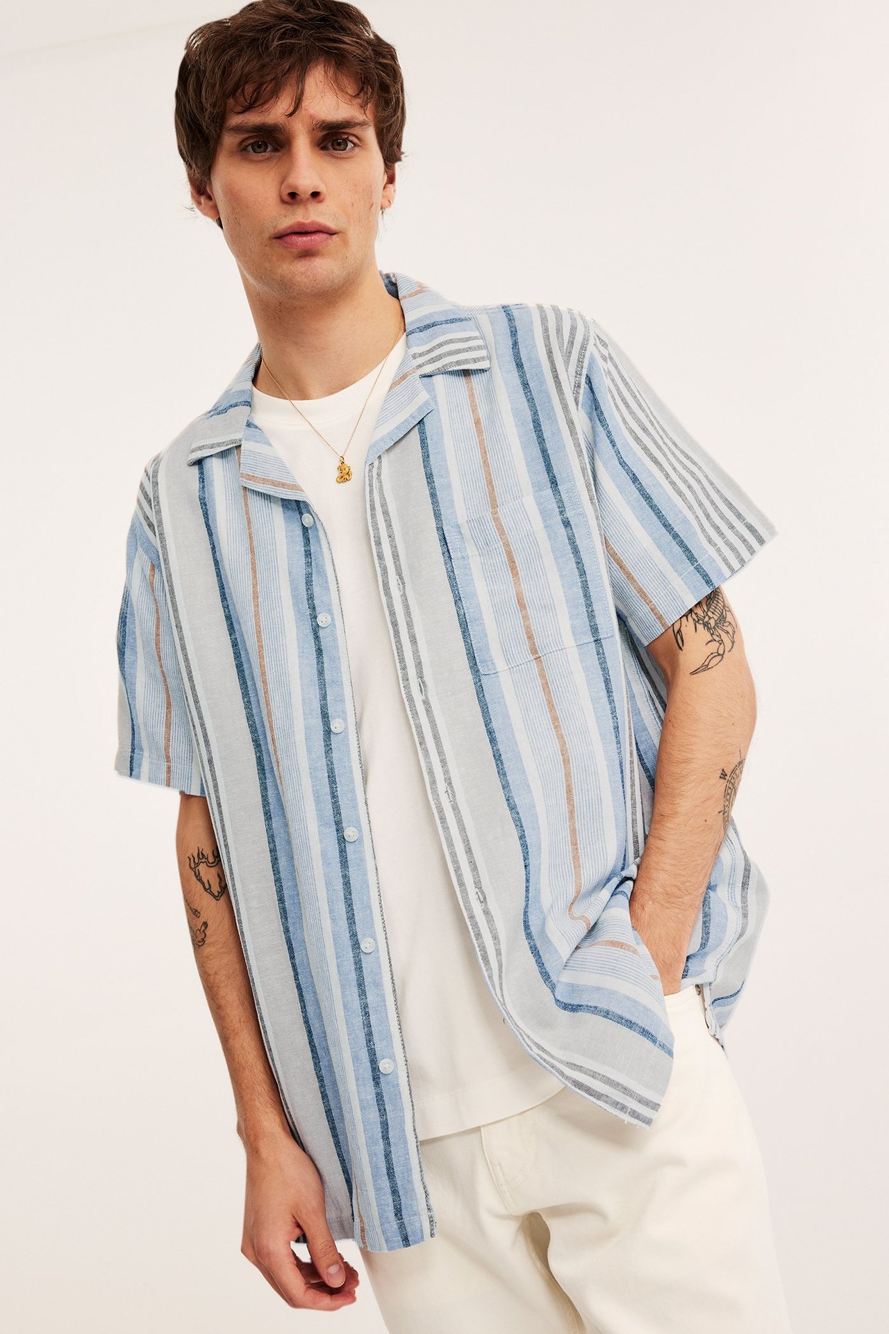 Edestä: Mies avoimessa siniraitaisessa lyhythihaisessa pellavasekoitepaidassa taskulla valkoisen t-paidan päällä.