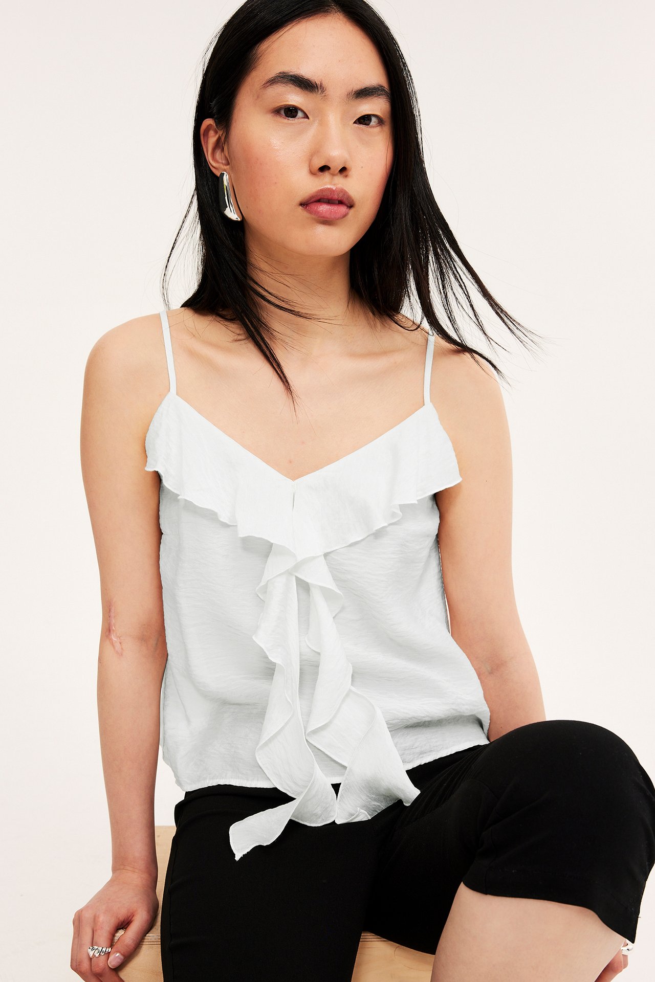 Framifrån: kvinna i offwhite volanglinne, svarta shorts, silverörhängen och silverring.