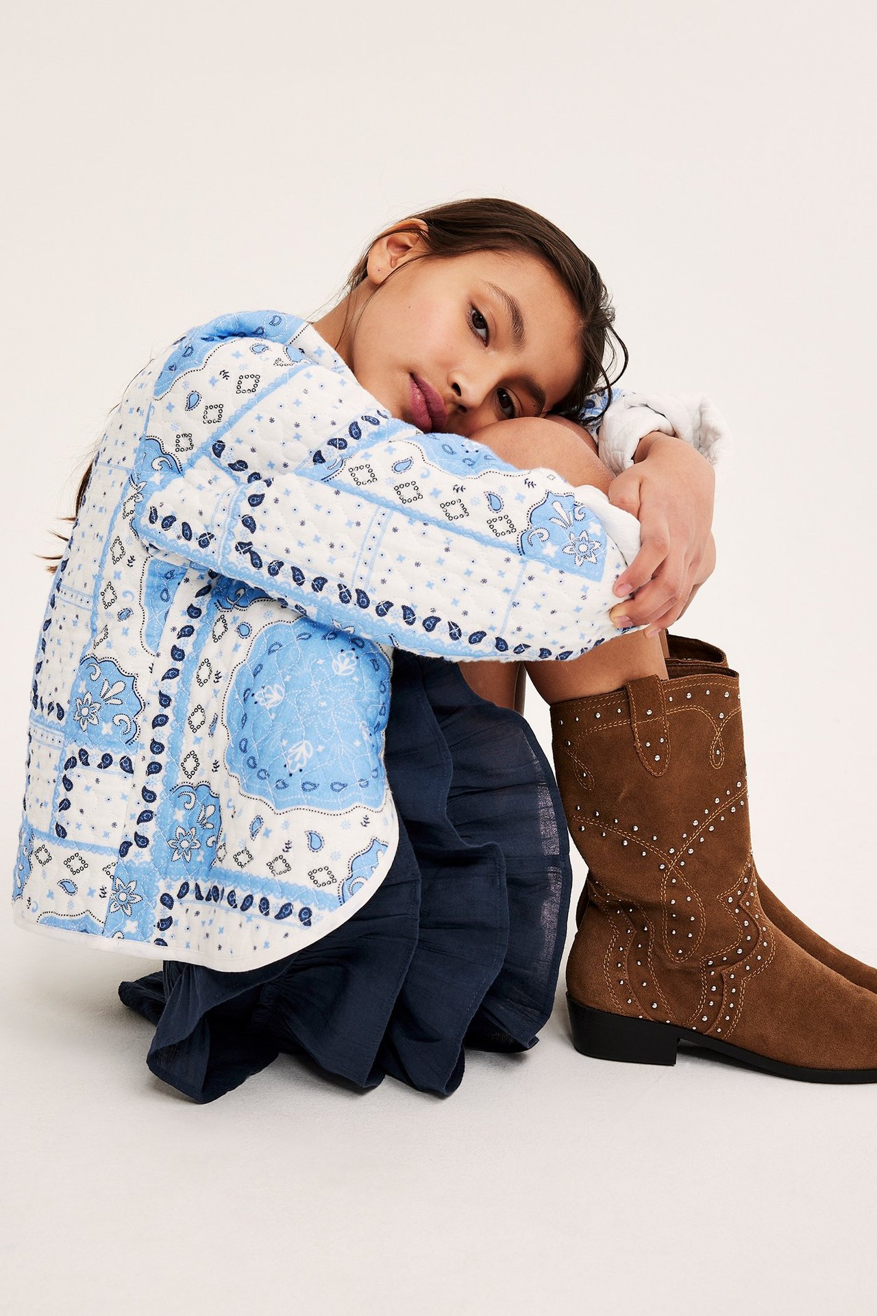 Forfra: et barn i mørkeblått vevd rysjeskjørt, hvit/blå mønstret jakke og brune naglestøvler.