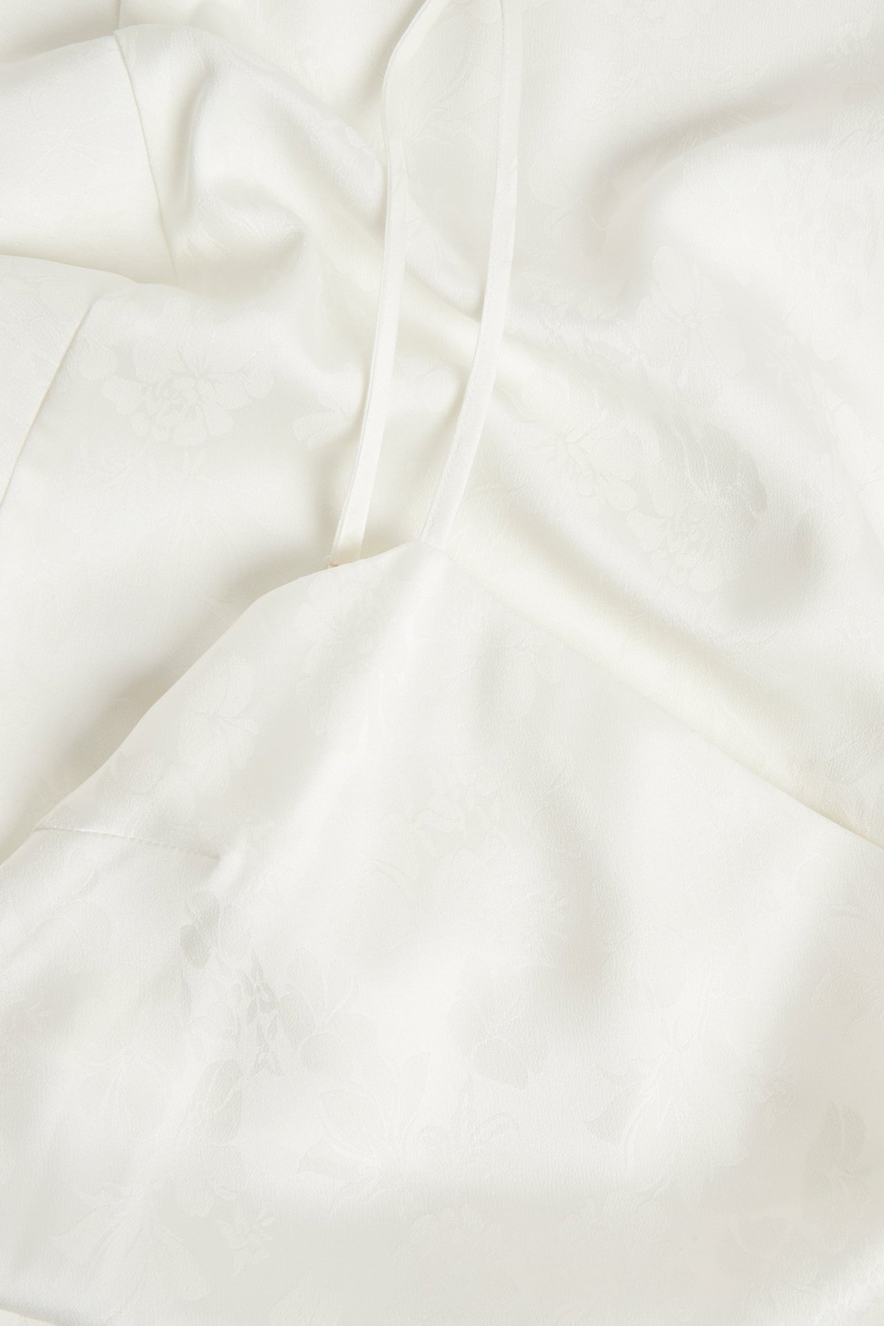 Zbliżenie na ecru asymetryczną sukienkę slip z żakardowym wzorem i cienkimi ramiączkami.