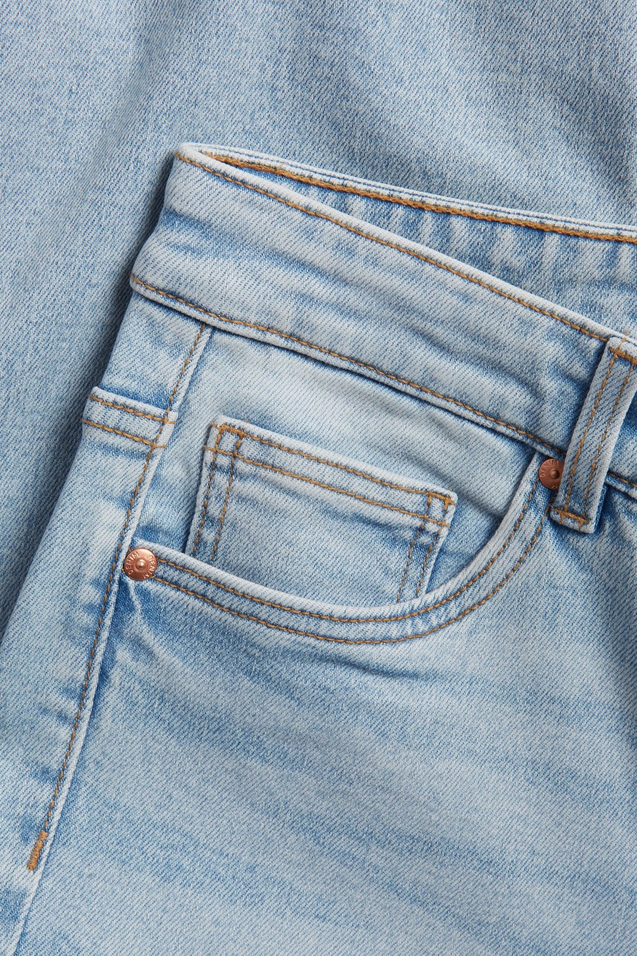 Zbliżenie na jasnoniebieskie jeansy straight z wysokim stanem, jasnym spranym efektem, kieszenią i nitem.