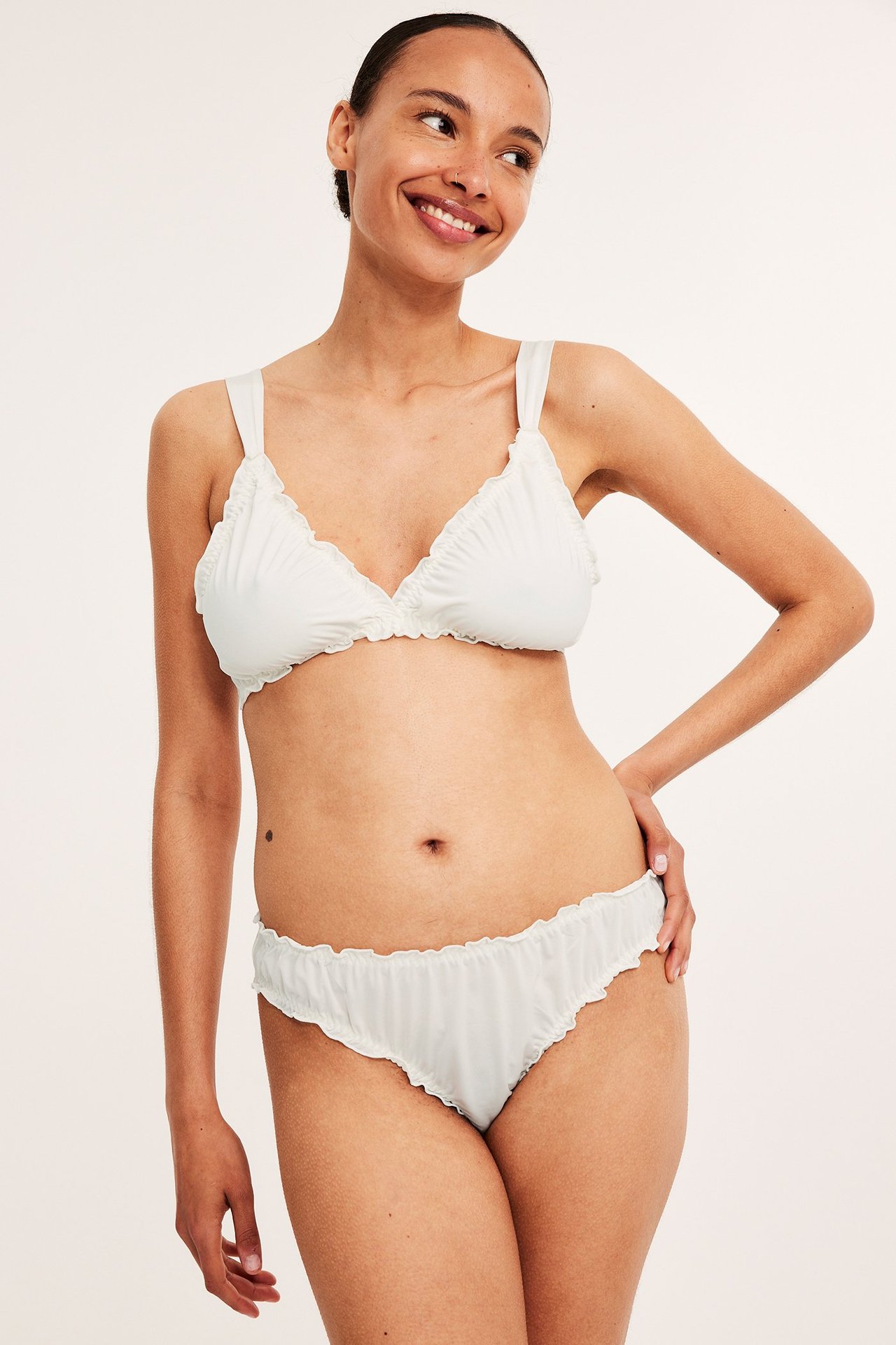 Frontbilde av en kvinne i offwhite rysjede brazilian-truser og matchende BH.