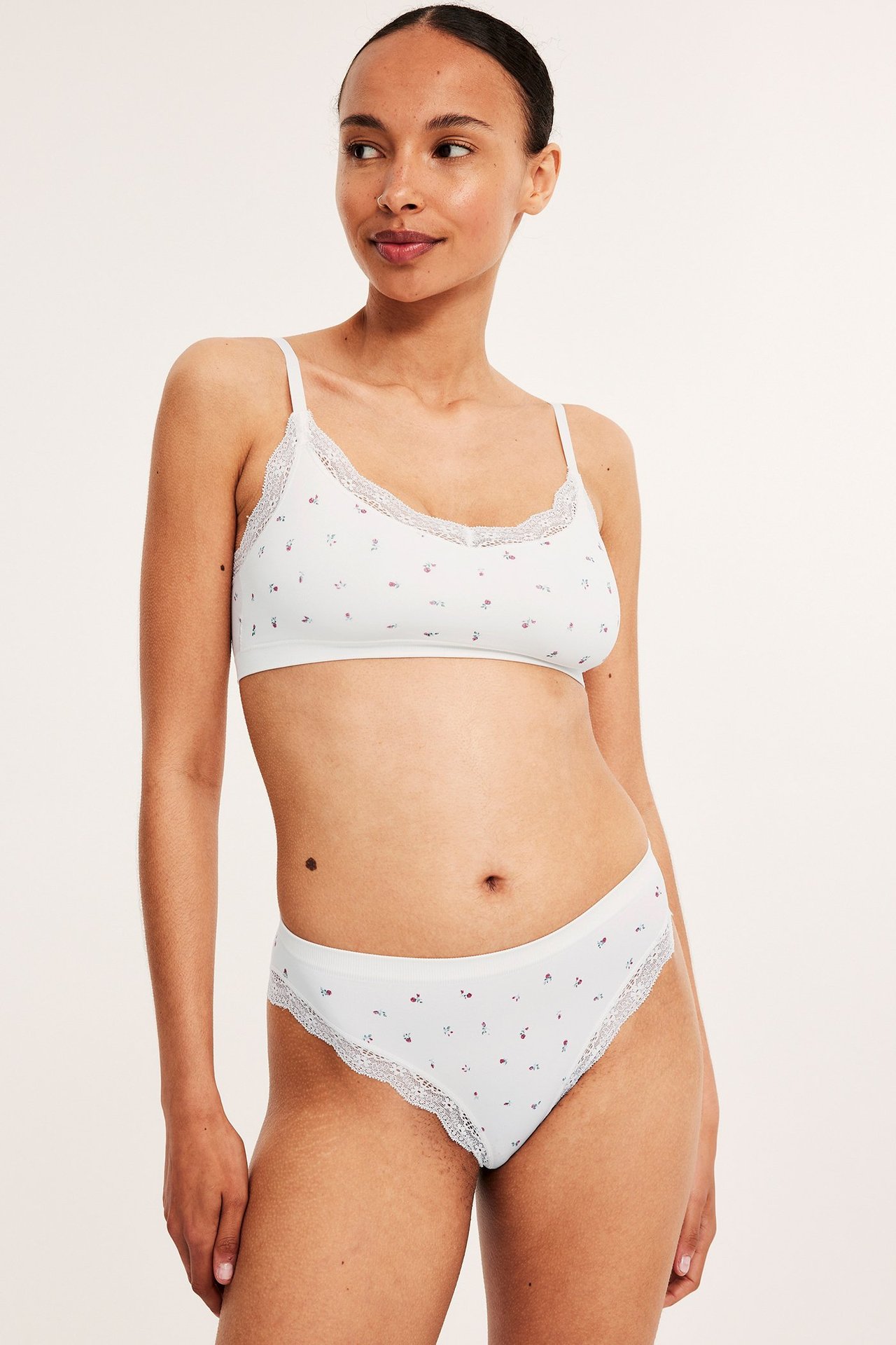 Frontbilde av kvinne i hvite sømløse truser med blomstermønster og blondekant, matchende BH.